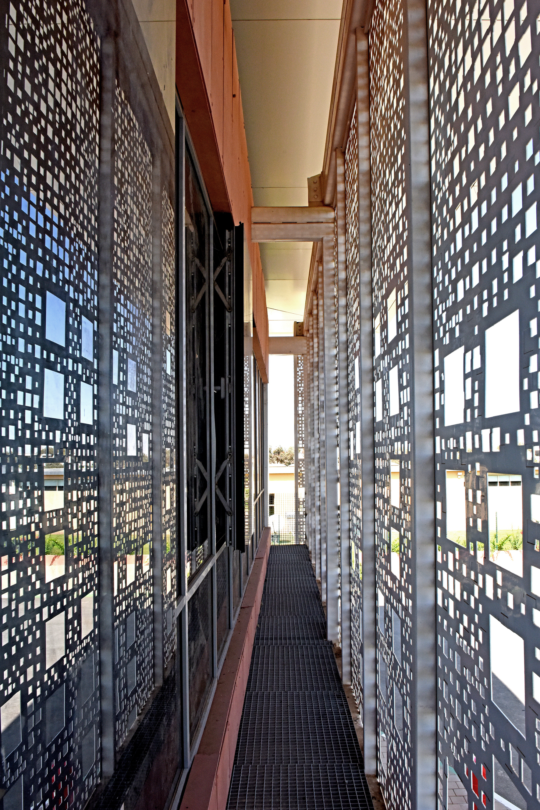Narrow service corridor lined with perforated metal screens creating dappled light patterns on the walkway
