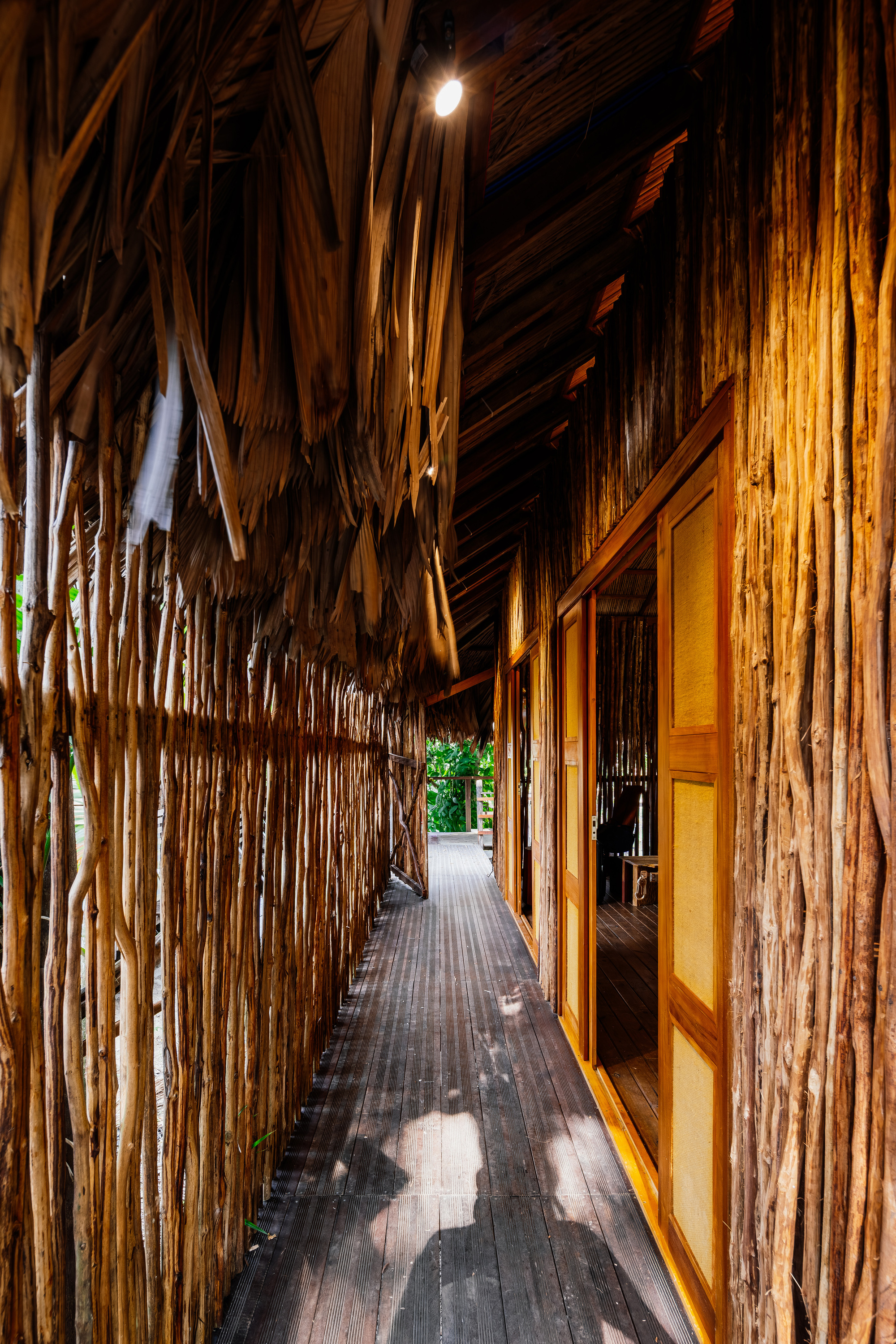 Interior corridor lined with vertical bamboo stalks and a thatched palm roof at night