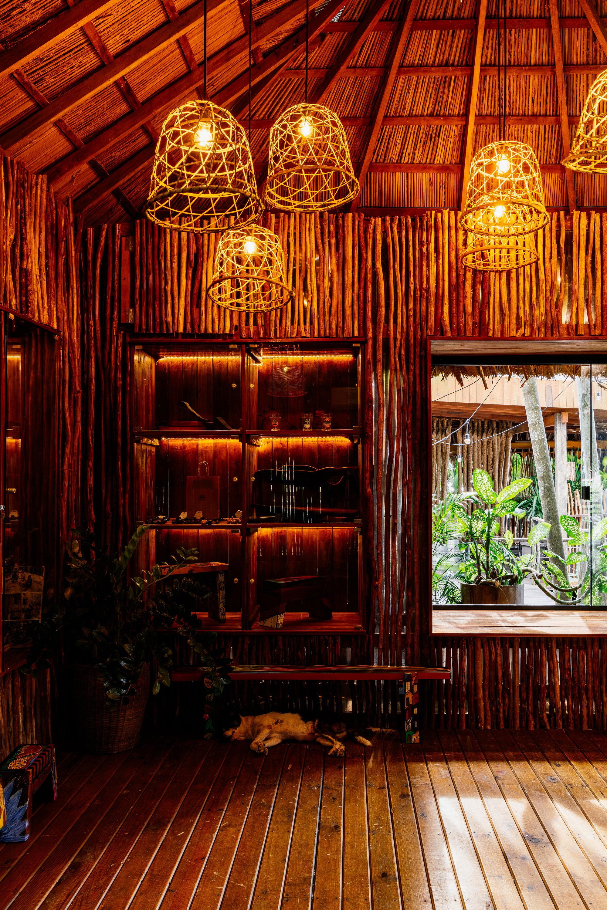Interior showing timber shelving unit beneath clustered woven pendant lights and a palm thatch ceiling