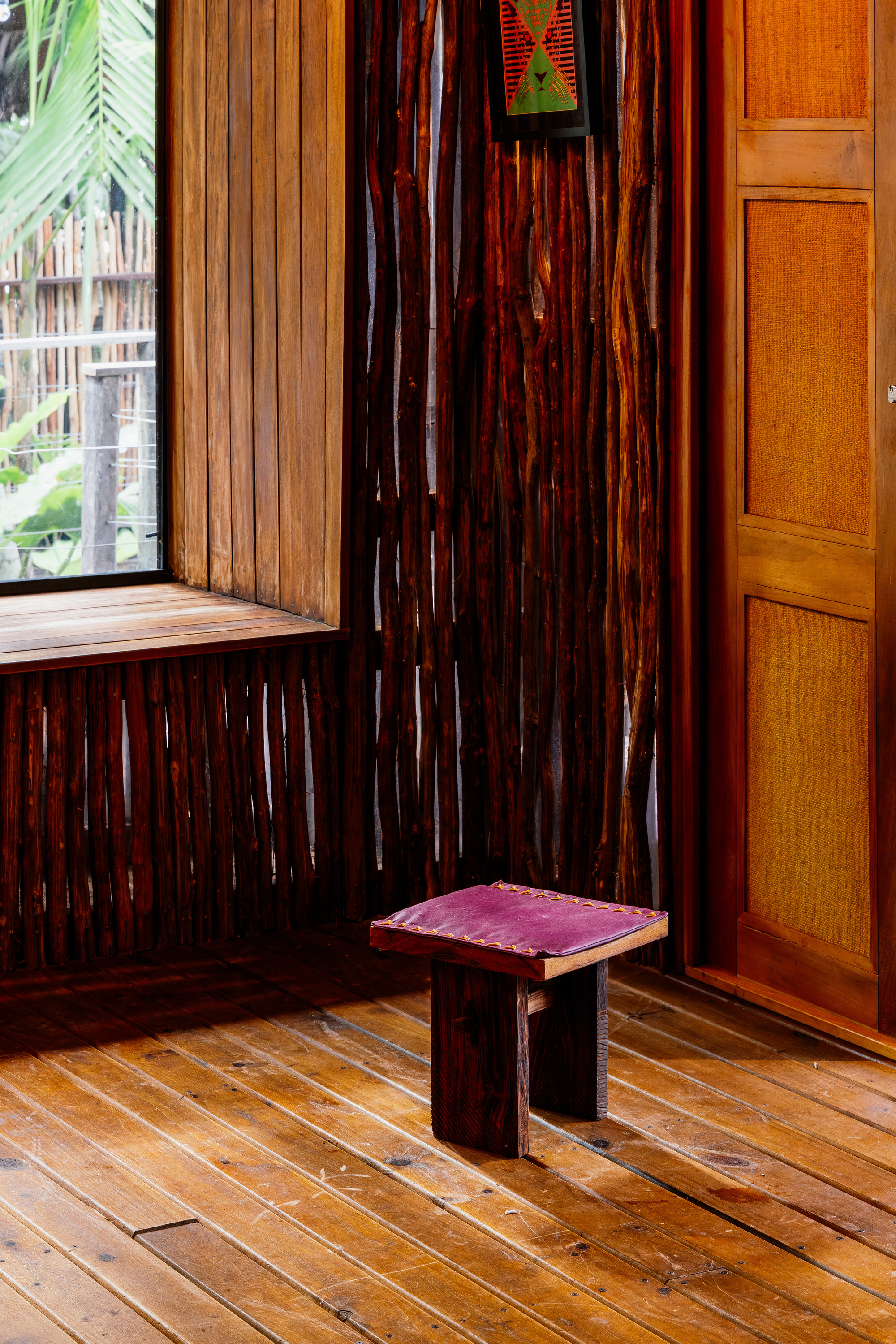 Corner detail with a low timber stool on plank flooring beside bundled bamboo walls