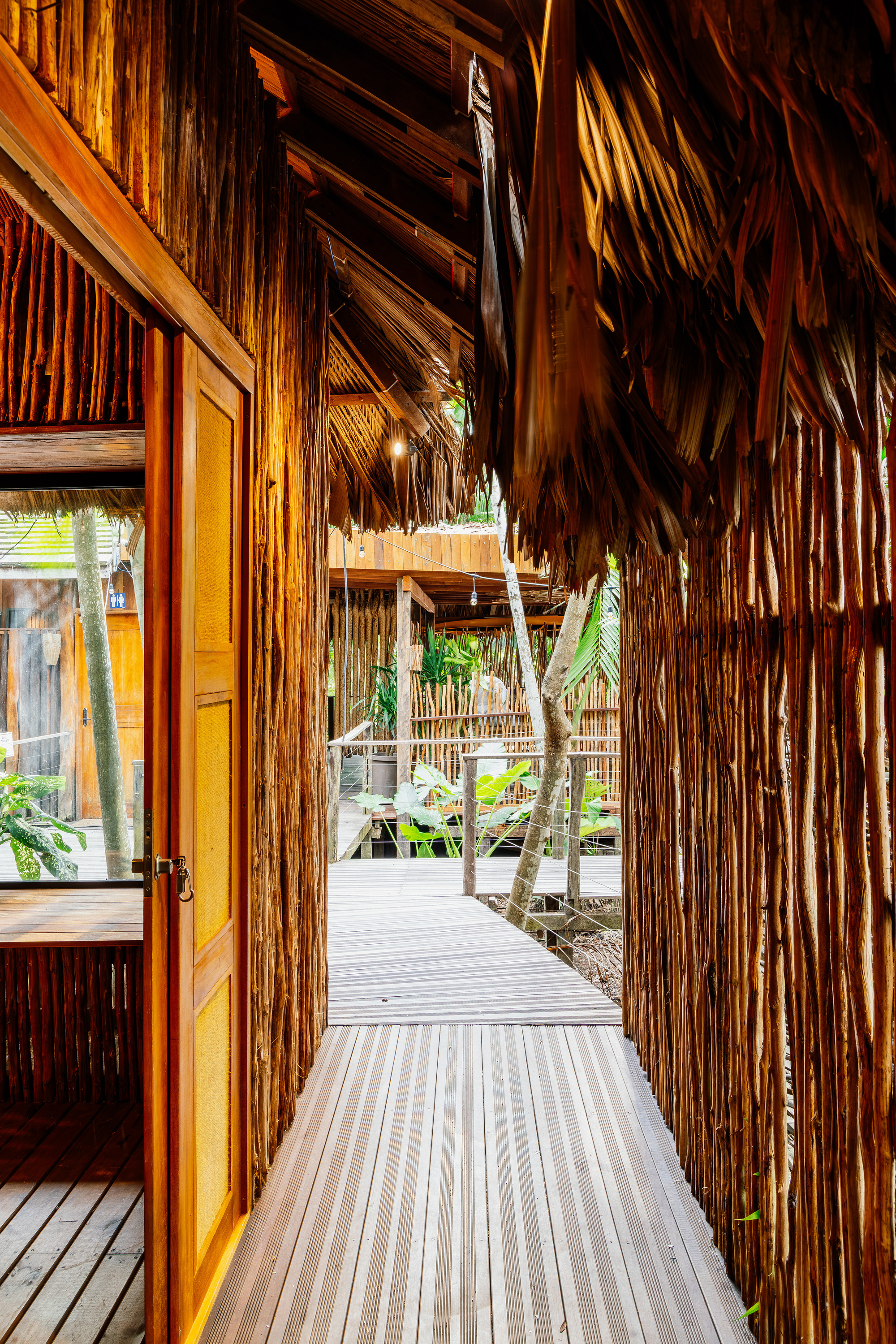 Covered walkway with vertical bamboo screens and palm thatch roof looking toward planted courtyard