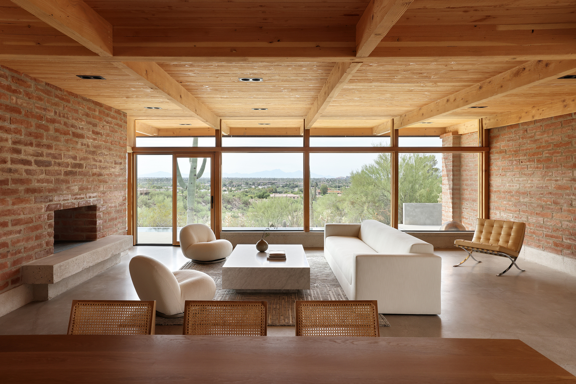 Living room with exposed timber ceiling beams and brick walls framing a panoramic window overlooking desert landscape