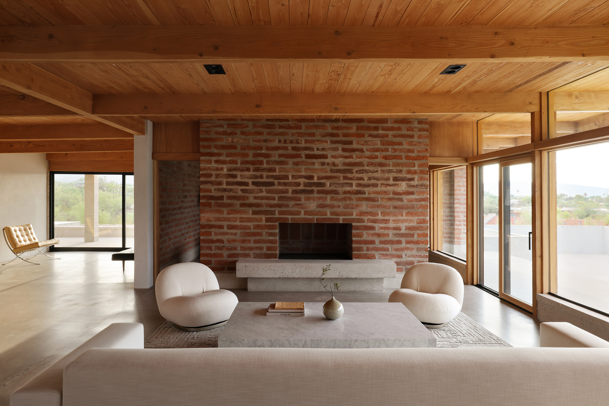 Red brick fireplace wall with concrete hearth beneath a timber plank ceiling with exposed beams