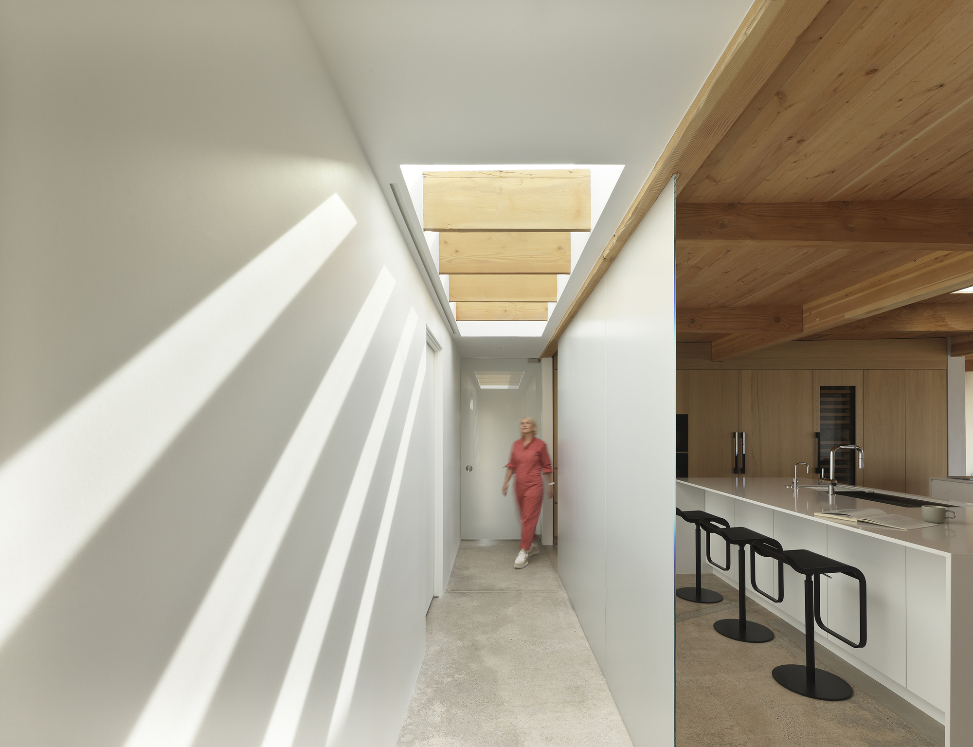 Corridor with overhead skylights casting striped shadows beside a white kitchen counter