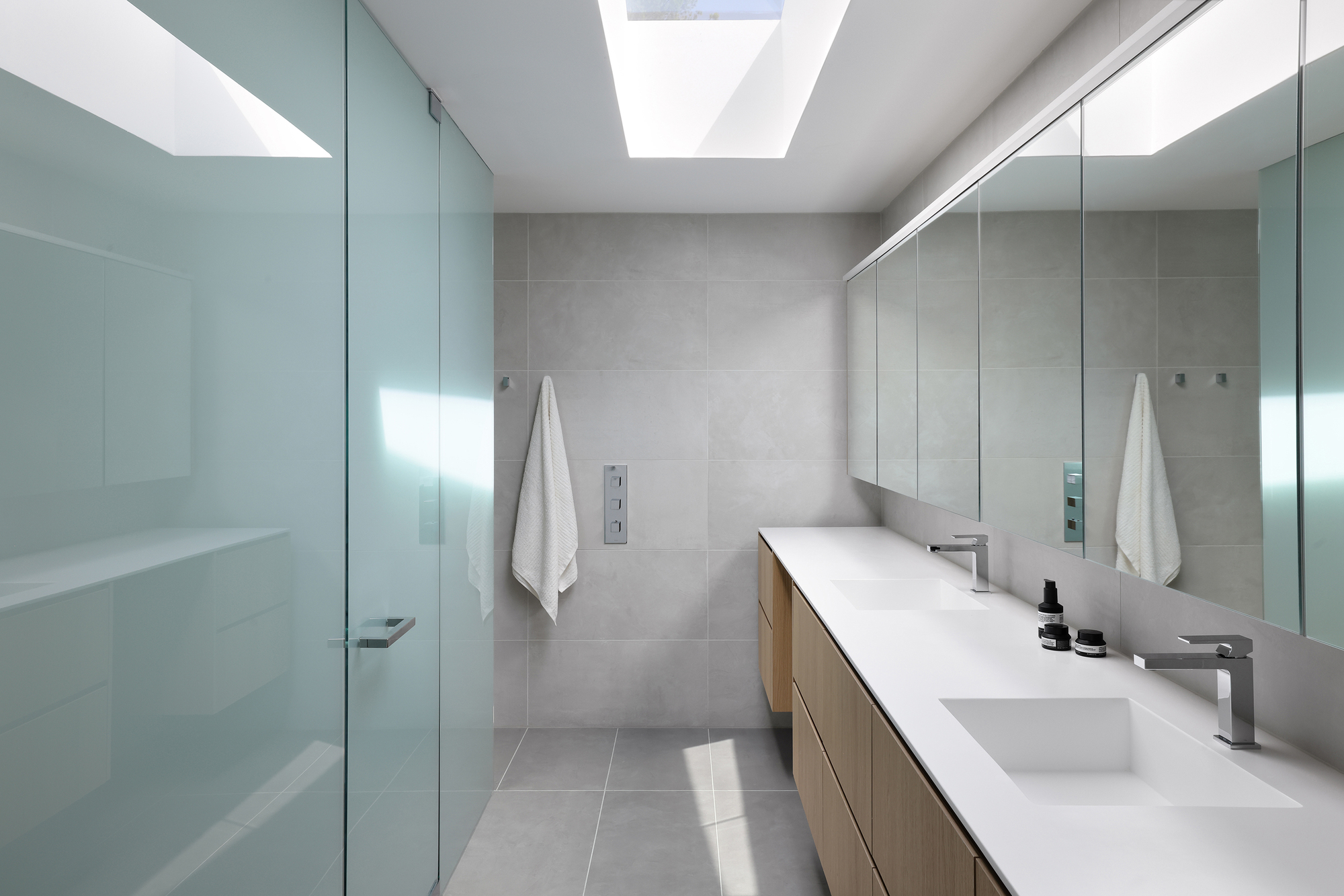 Bathroom with double vanity and frosted glass shower enclosure lit by a skylight