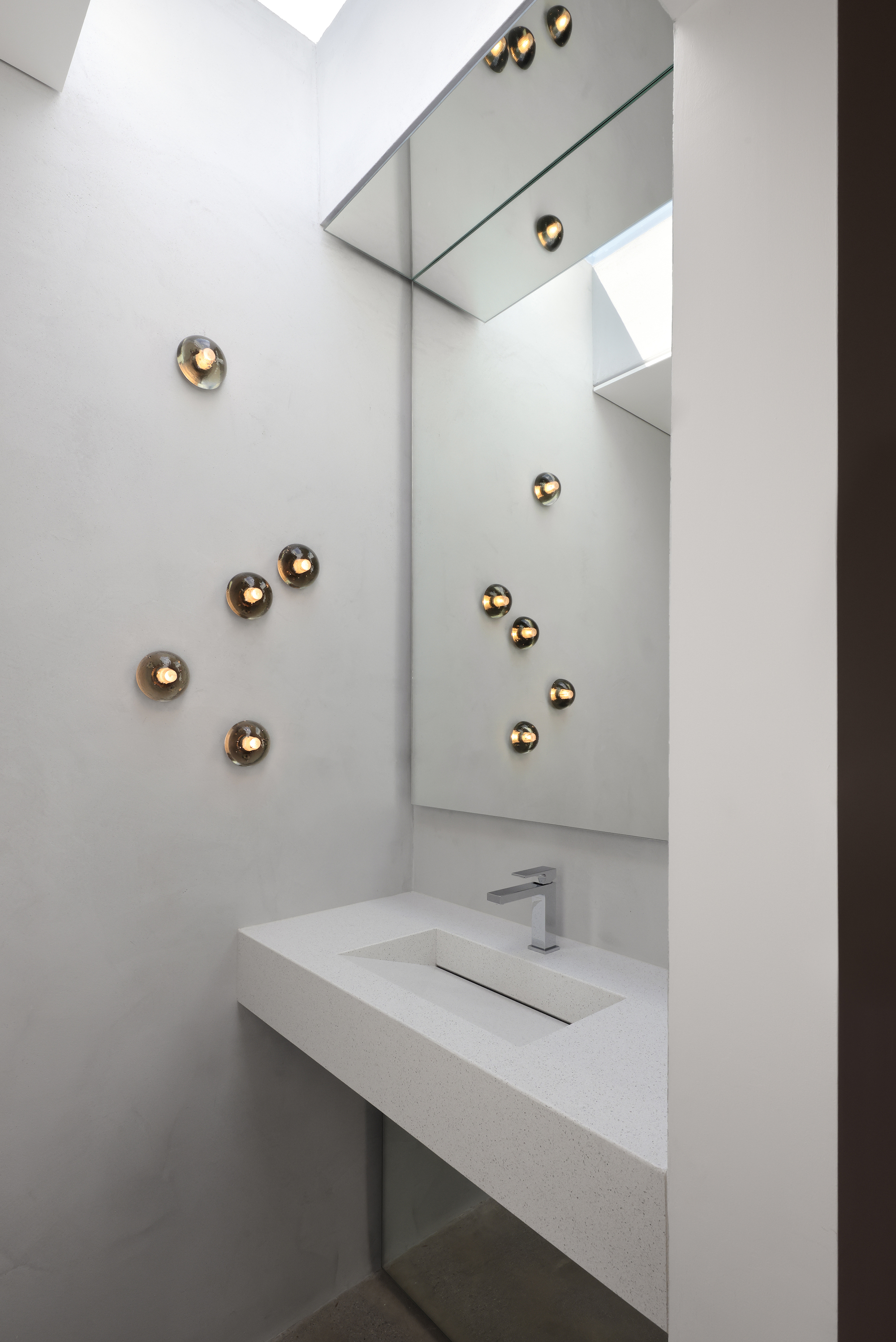Powder room with white floating vanity, angled mirror, and spherical brass sconces scattered across the wall