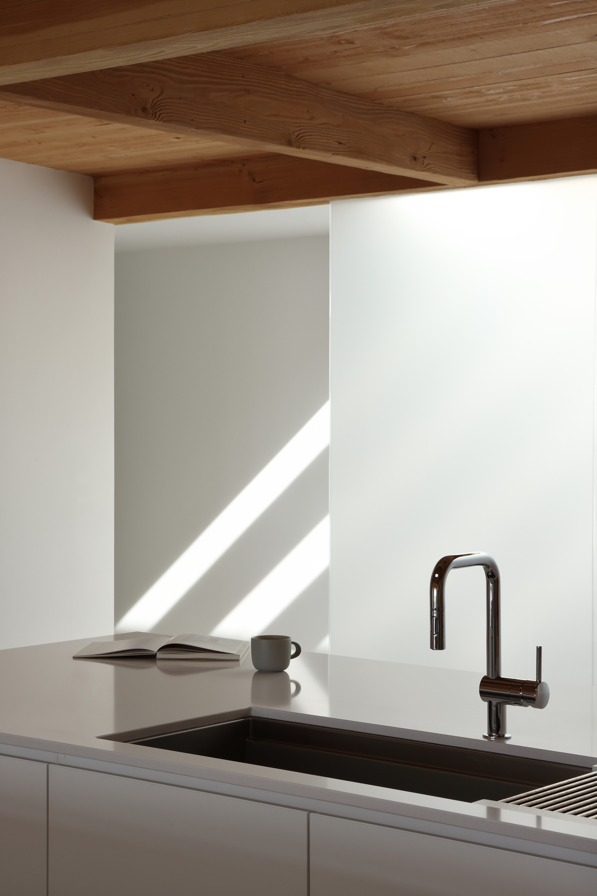Kitchen counter with black undermount sink and dark faucet beneath timber plank ceiling in morning light