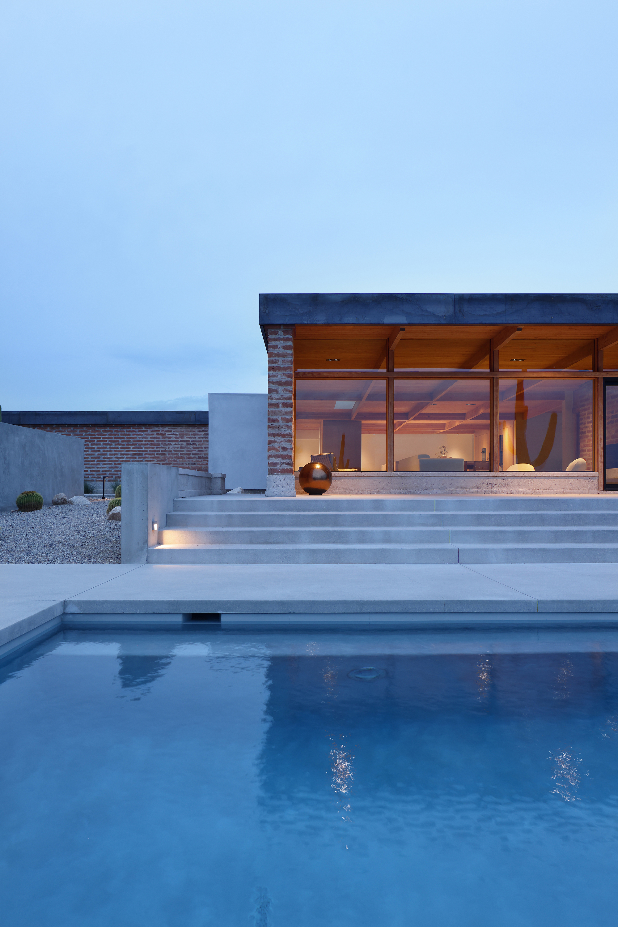 Stepped concrete terrace rising from the pool to the glazed living space at twilight