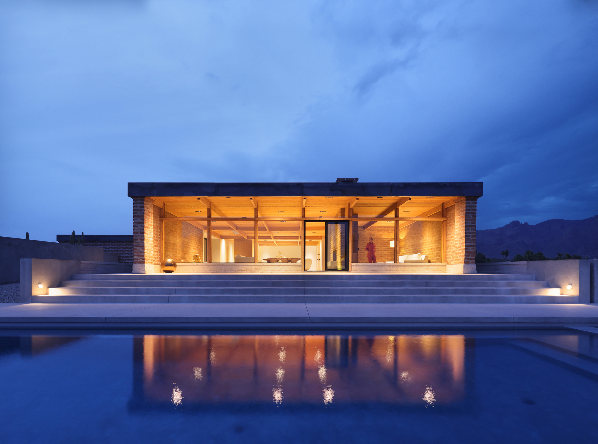 Glass-walled pavilion with exposed timber beams reflected in the still pool at night