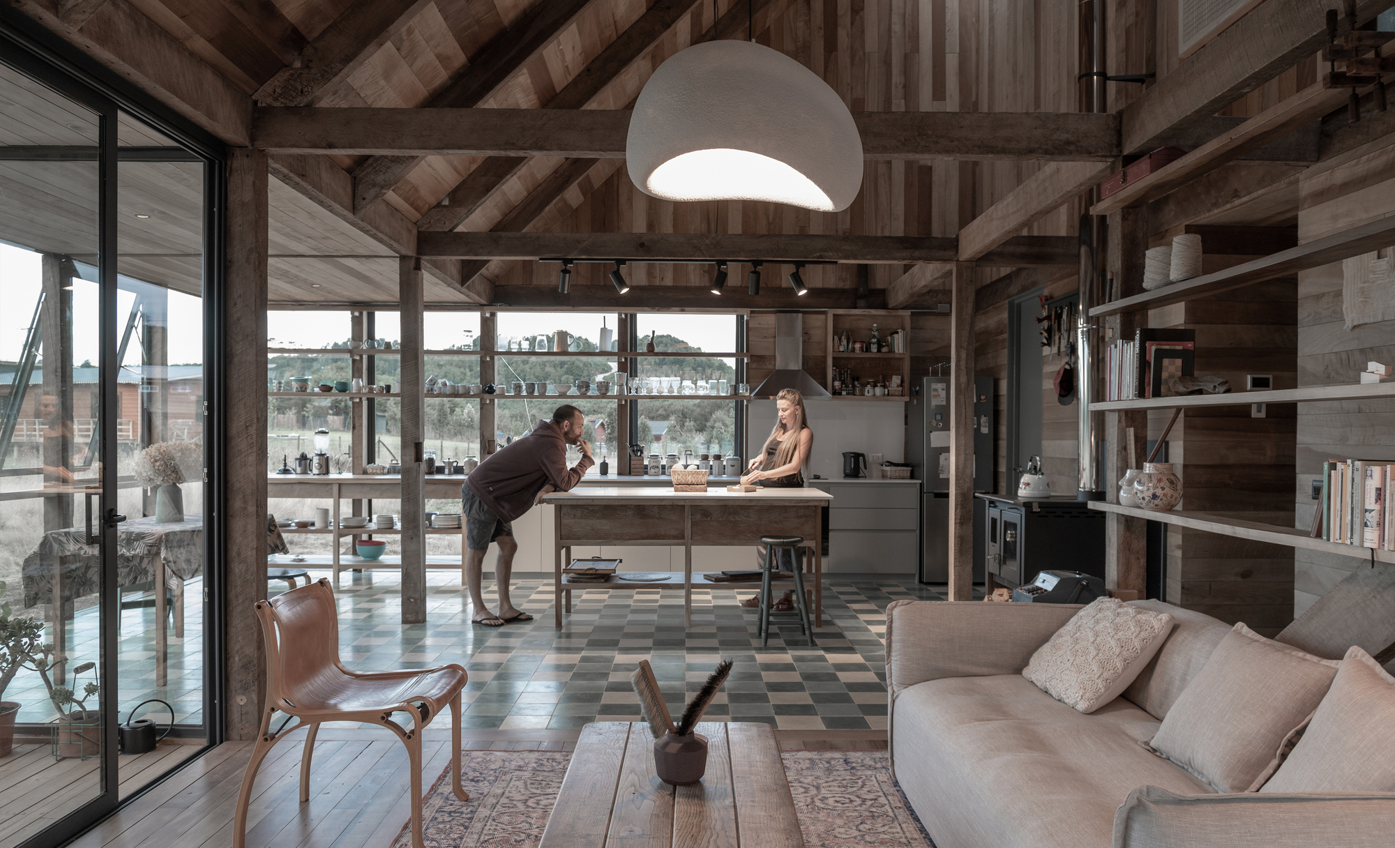 Open-plan living area with exposed timber beams, patterned floor tiles, and two people at the island