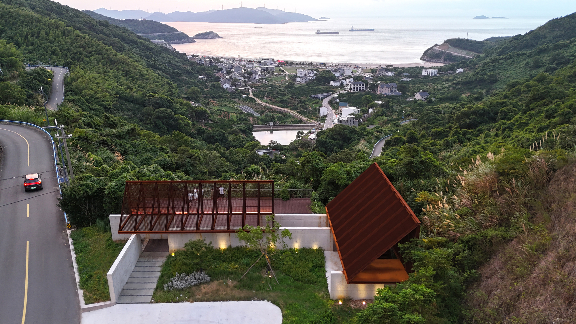 Aerial view of two tilted roof volumes on a hillside overlooking the bay at dusk