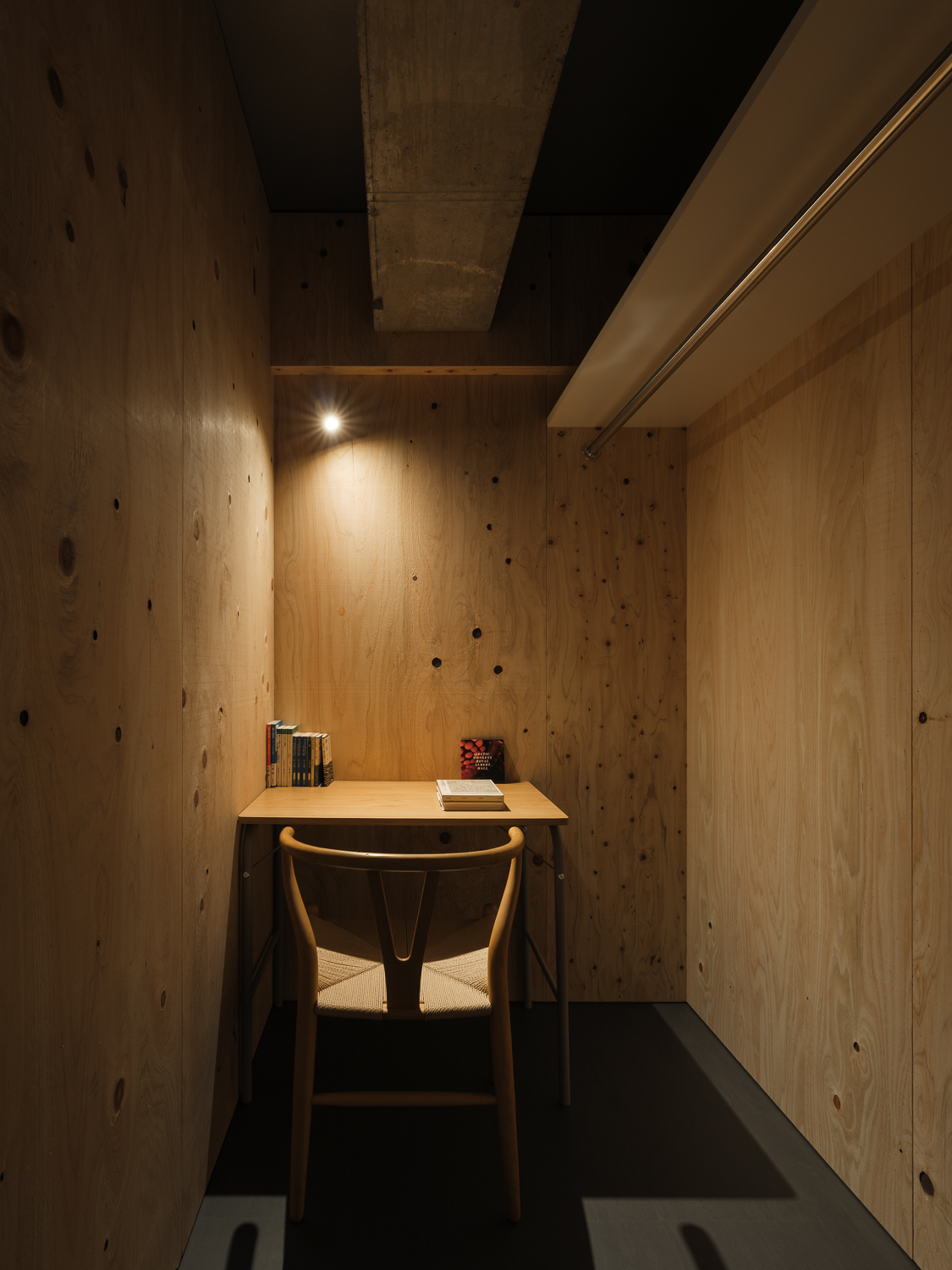 Small plywood-clad study nook with wall-mounted desk and single chair beneath warm overhead lighting