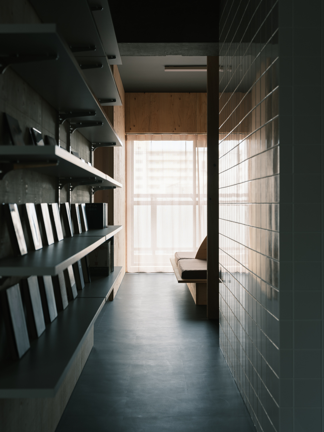 Dark corridor with open shelving along one wall leading toward a sunlit doorway