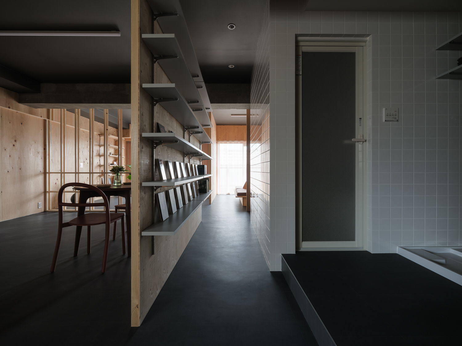Narrow passageway with grey tile walls and floating steel shelves lined with bottles