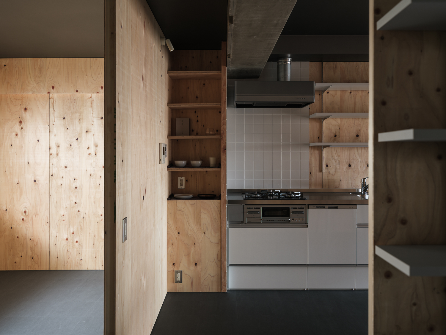 Compact galley kitchen with white tile backsplash and plywood storage shelving in low light