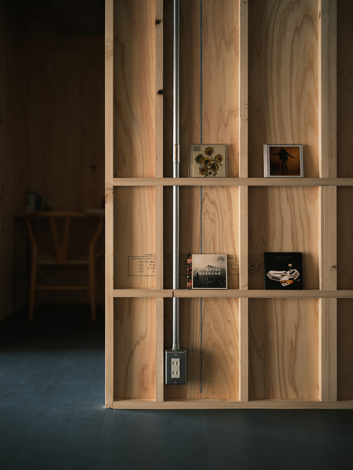 Plywood shelving unit with vertical conduit and electrical outlet displaying small framed photographs