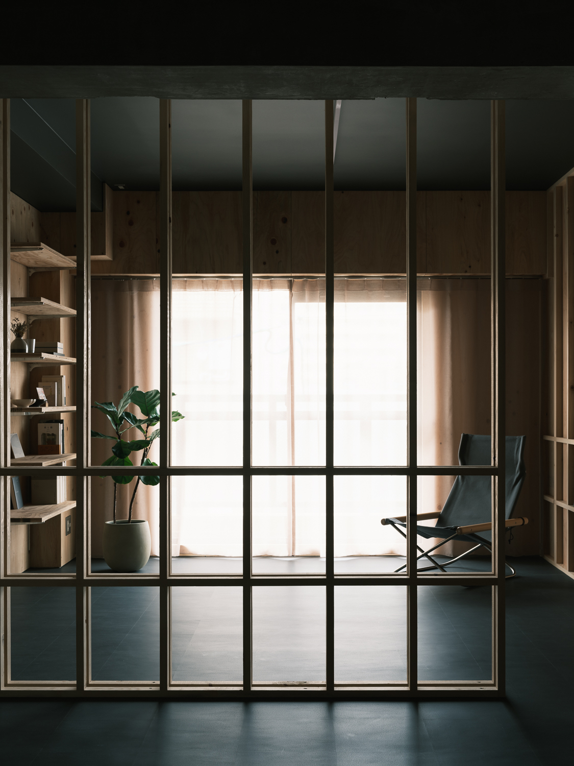 Full-height steel and glass partition framing a view into a timber-lined space with daylight filtering through curtains