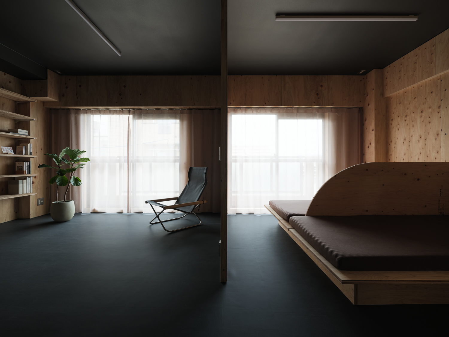Open living area with timber walls, dark grey rubber flooring, and sheer curtains over glazed openings