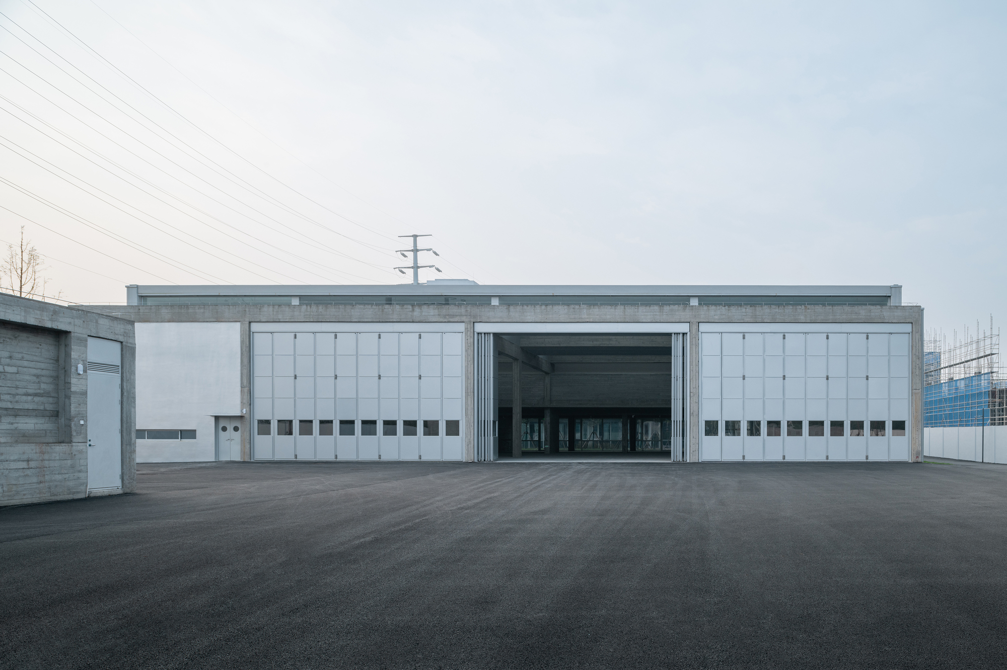 Symmetrical facade with sliding metal doors flanked by white panel walls beneath overhead power lines