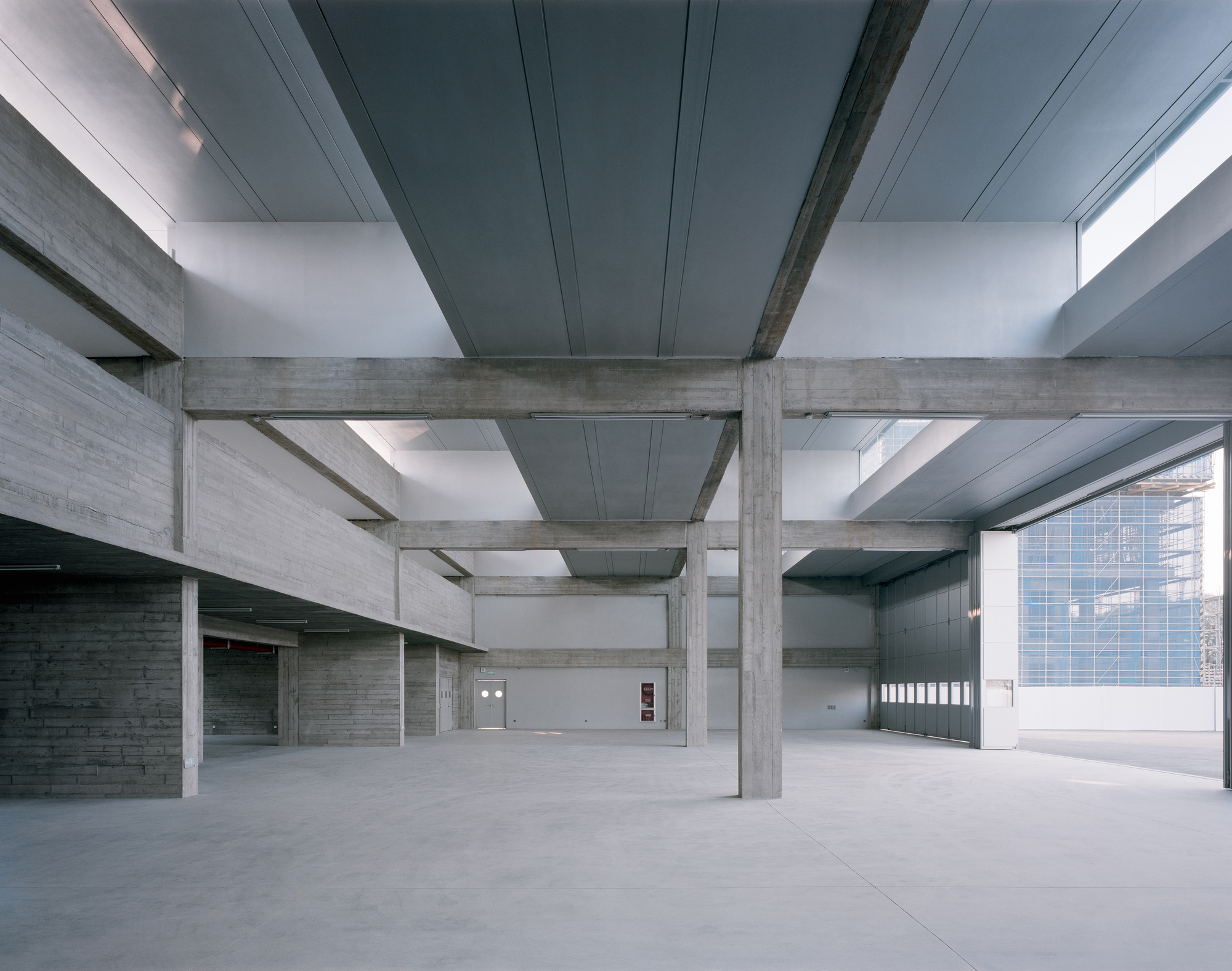 Interior space with board-formed concrete beams and metal ceiling panels lit by clerestory windows