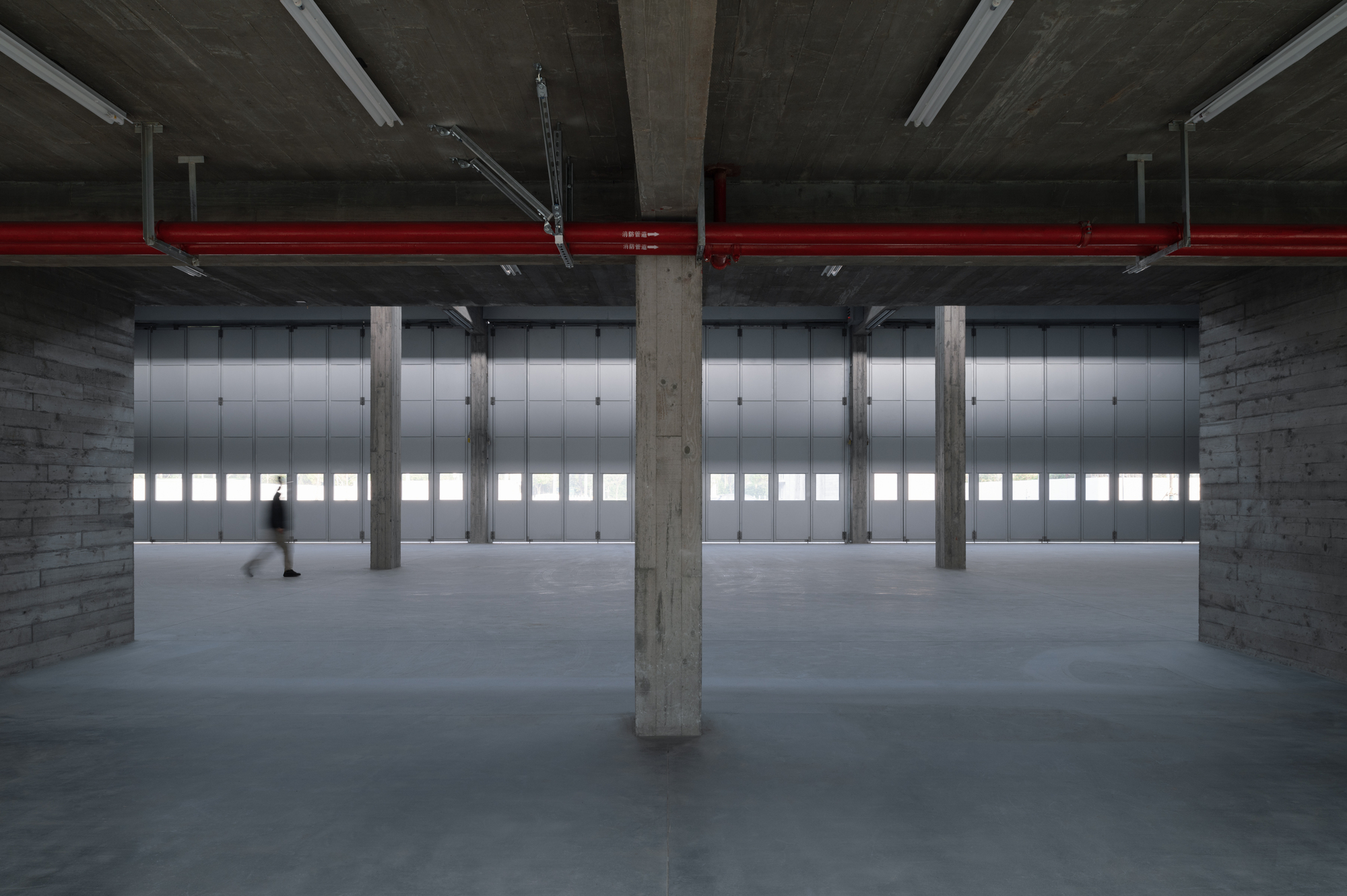 Raw concrete columns and exposed ceiling in an open floor with translucent glazed panels along the perimeter