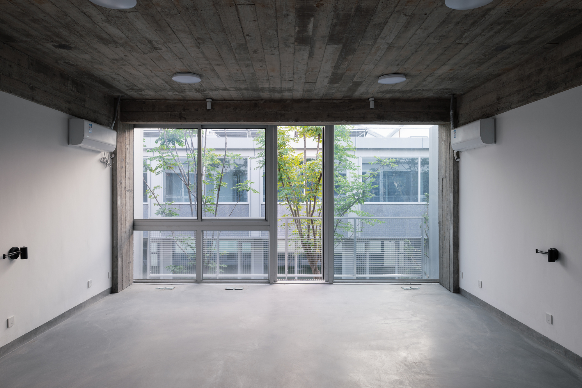 Full-height glazing with view to planted courtyard and neighboring buildings through a board-formed concrete frame