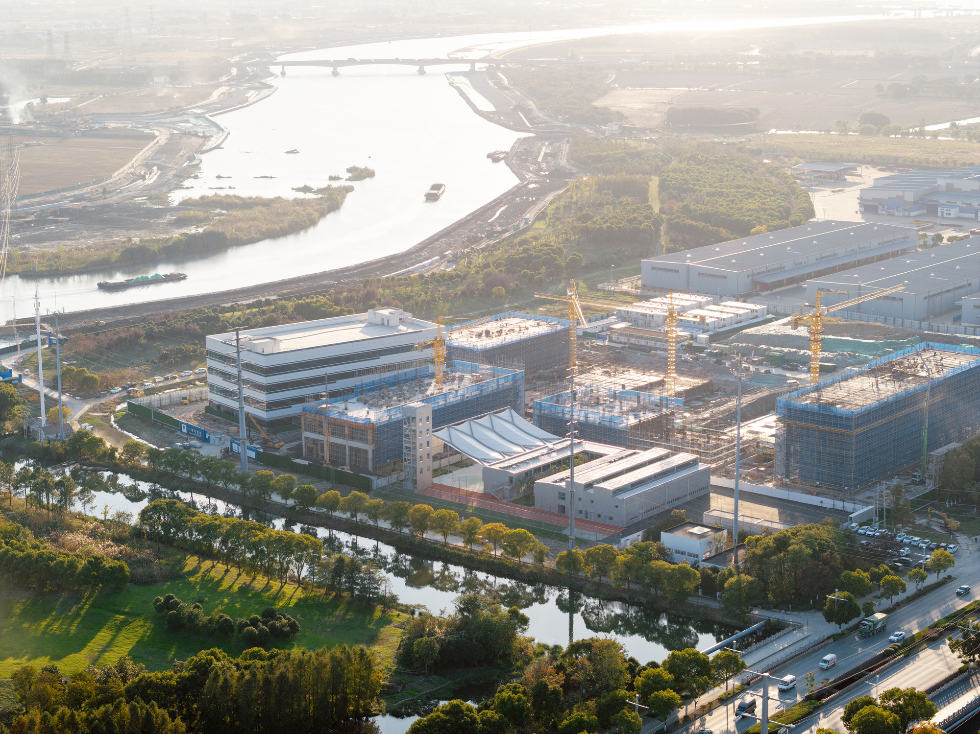 Aerial view of the construction site with tower cranes beside a meandering river at dawn