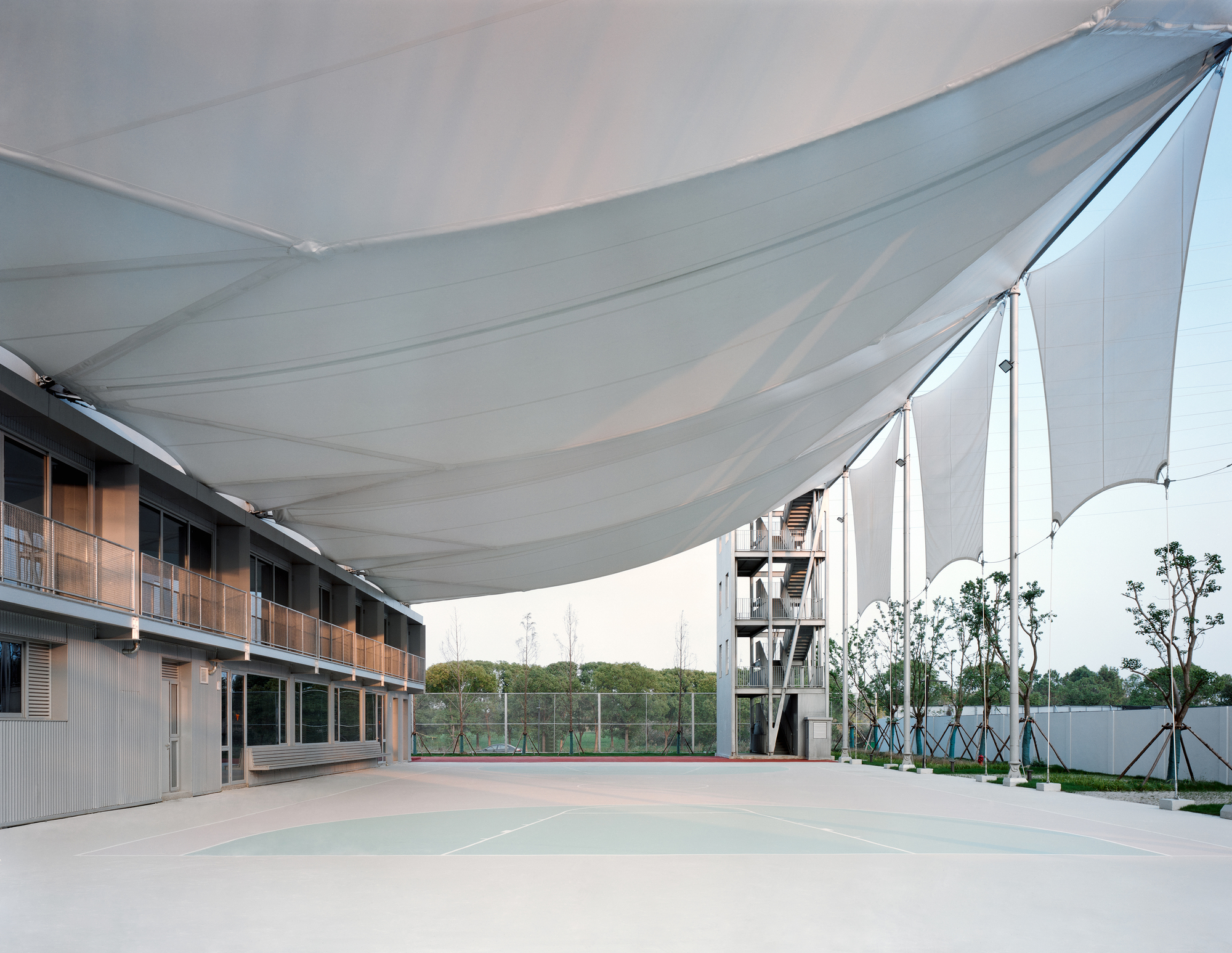 Courtyard with tensile fabric canopy stretched between residential blocks and a planted perimeter fence