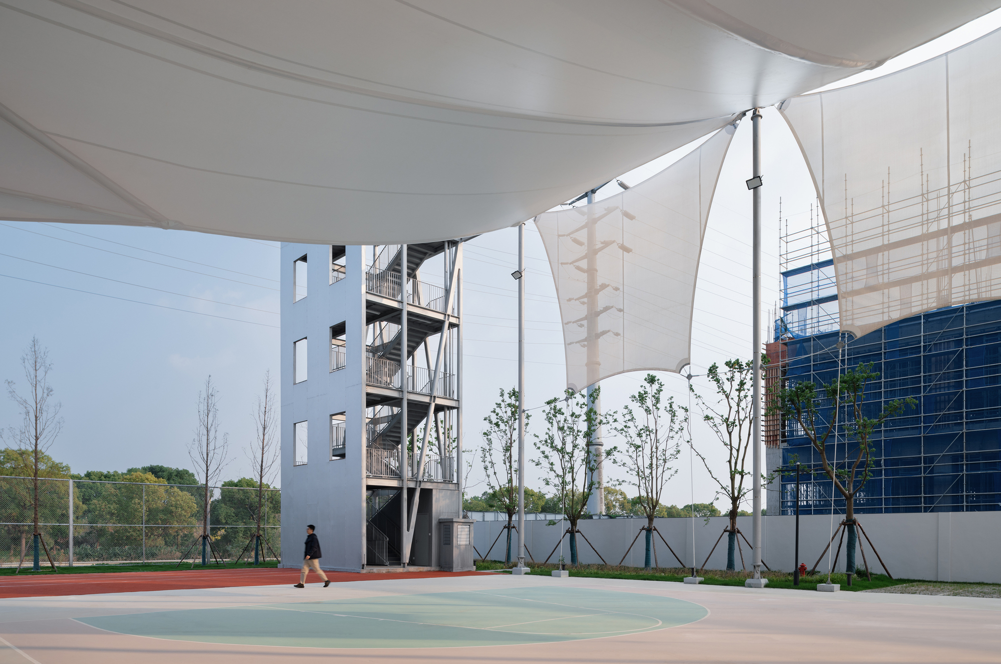 Exterior courtyard beneath a fabric canopy with a person walking across the tinted concrete surface