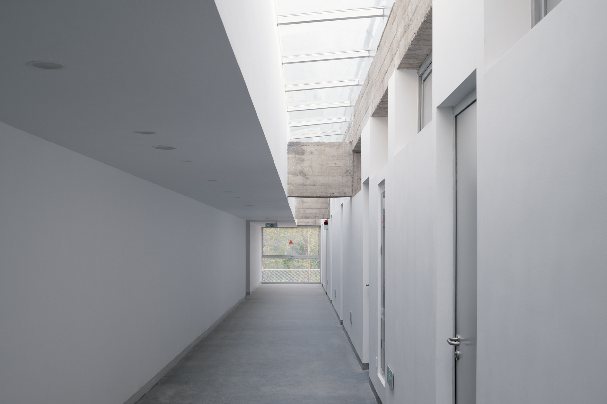 White interior corridor with linear skylight and exposed concrete beam under natural daylight