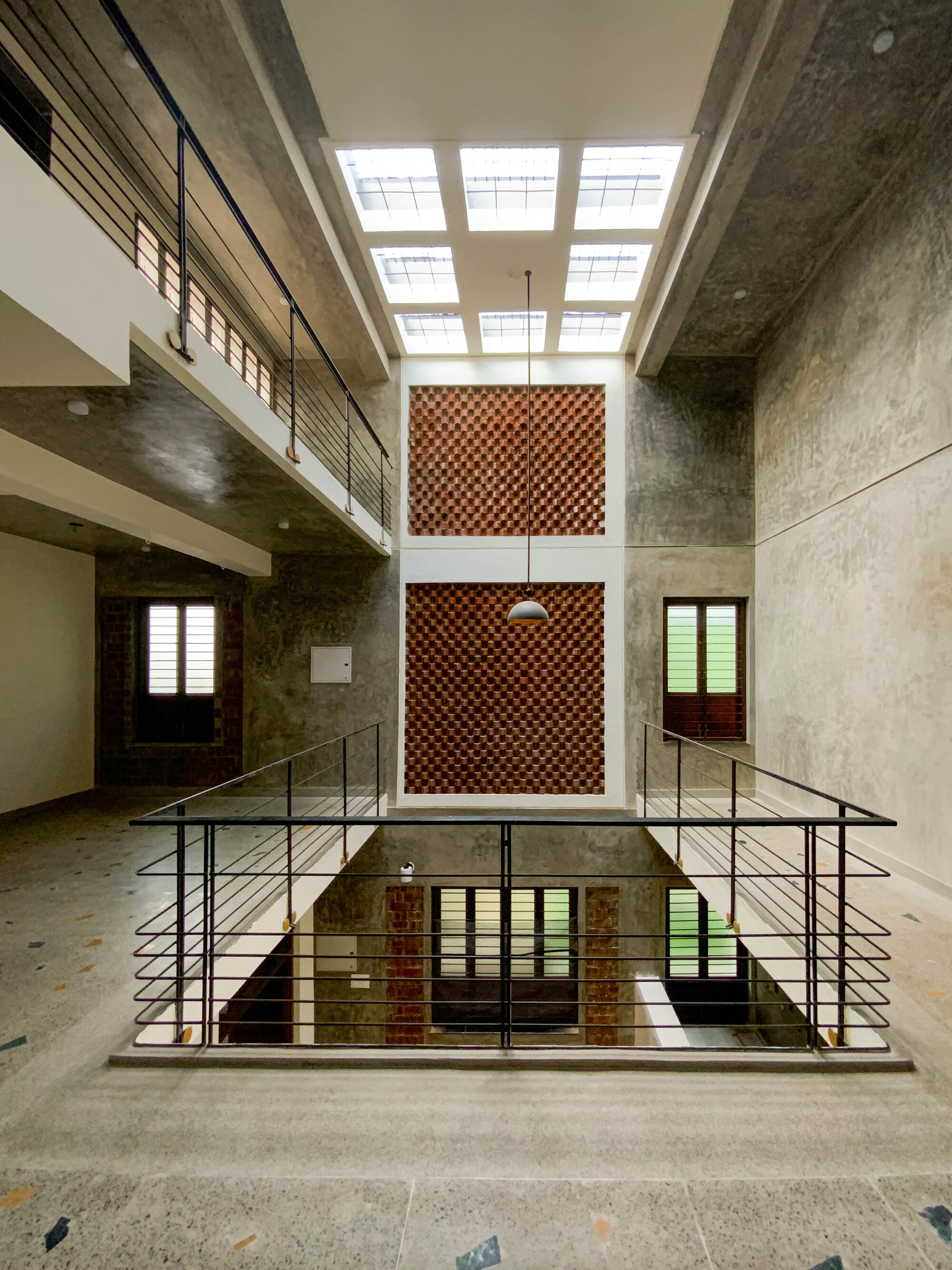 Triple-height atrium with central perforated brick screen, steel railing and skylights overhead