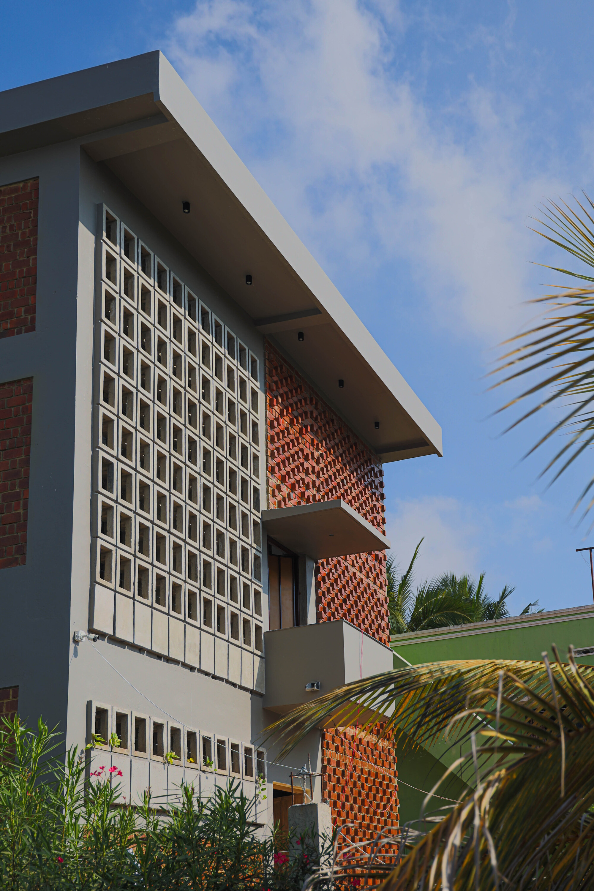 Side view of the facade showing perforated brick panels and white concrete block screen with palms
