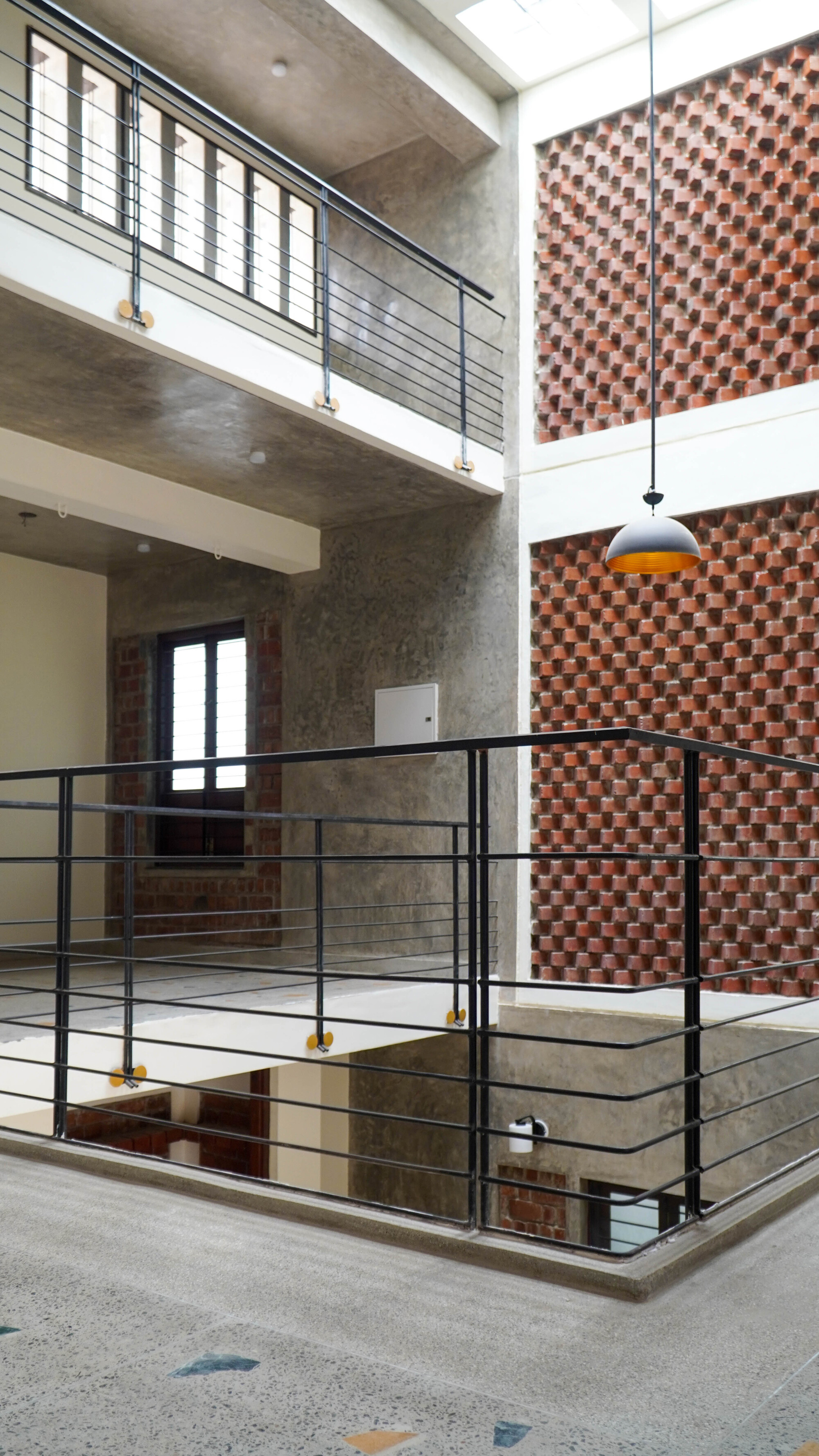 Metal railing around the central stairwell with a pendant light and chequered brick wall behind
