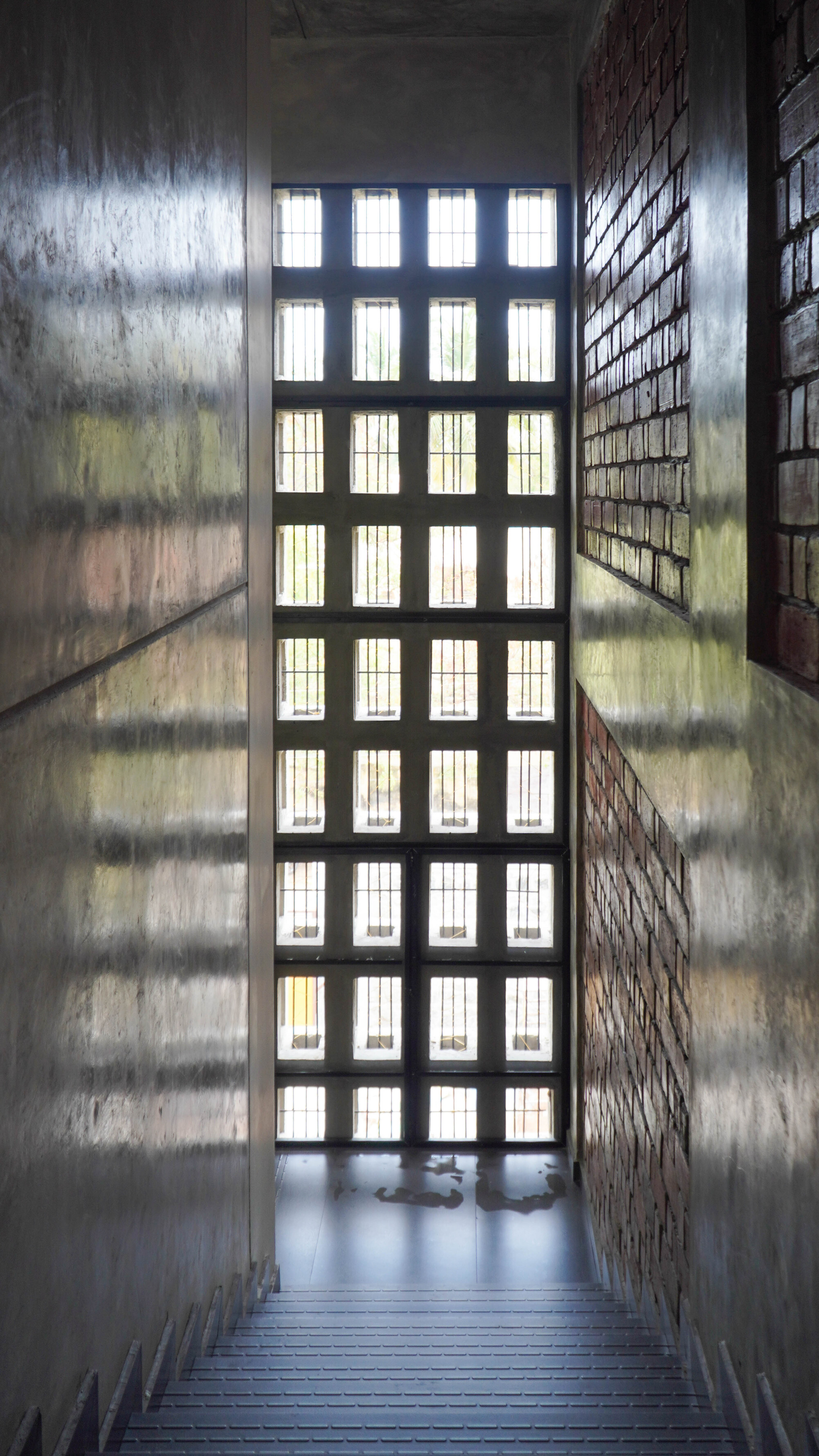 Staircase with gridded window wall casting shadows on concrete side walls and brick screen