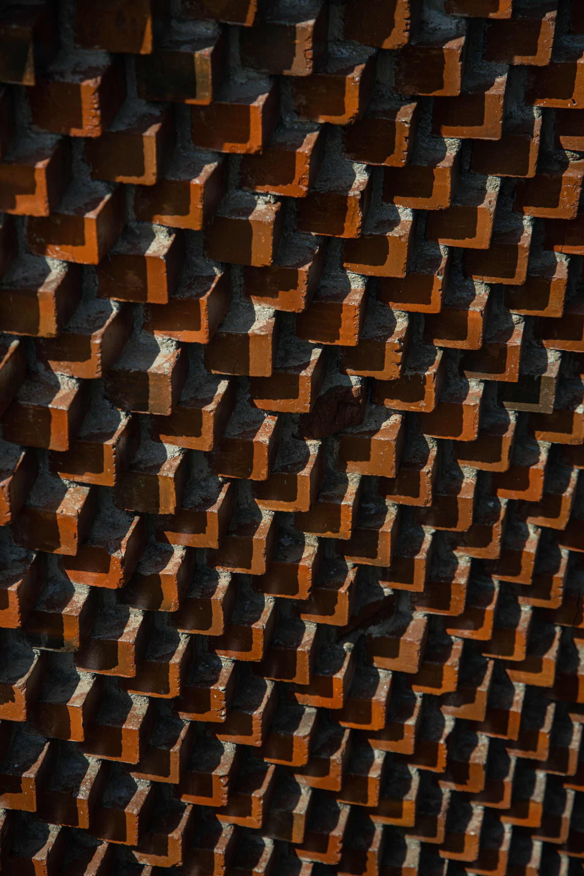 Close-up of projecting terracotta bricks in a stepped diagonal pattern creating shadow play