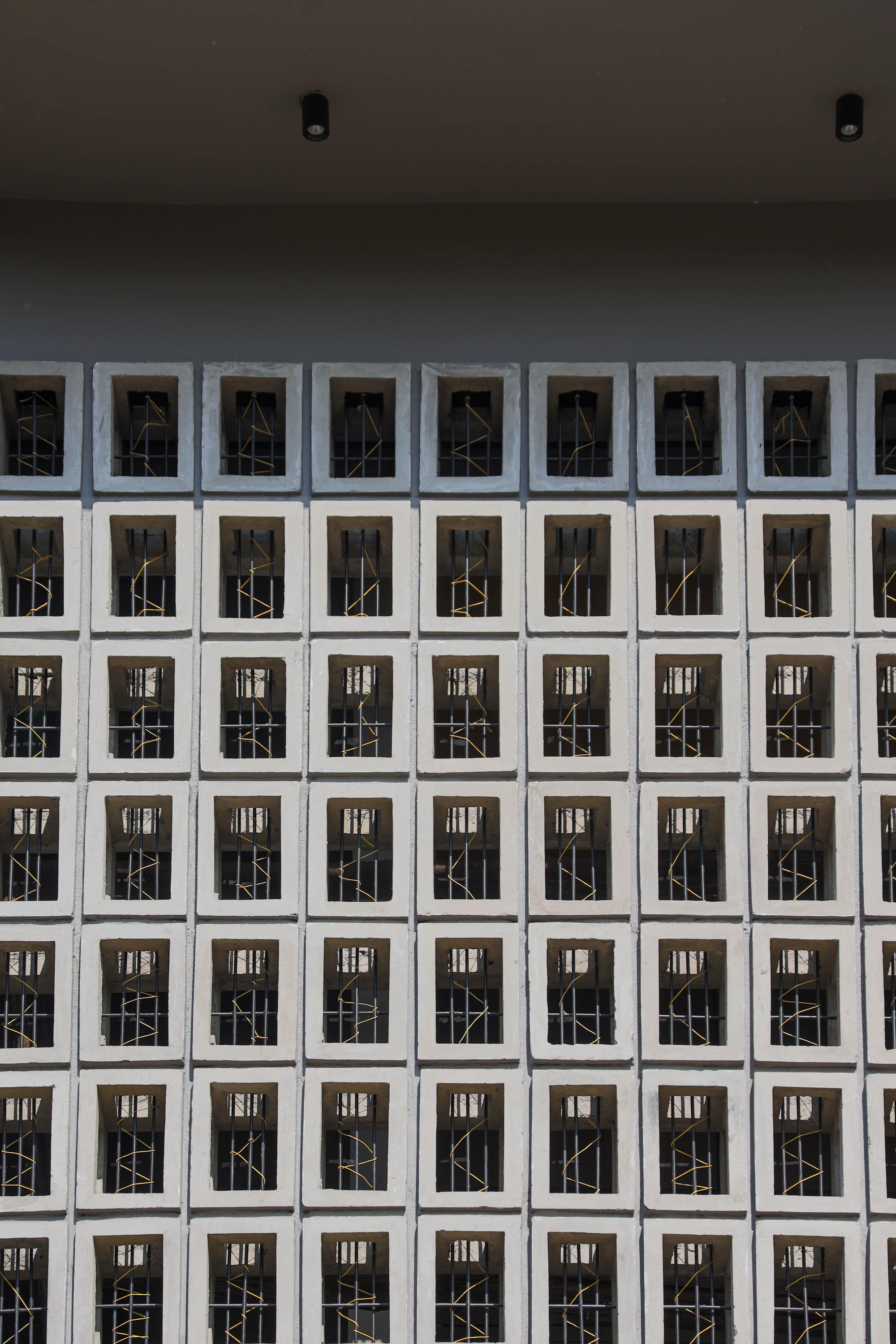 Grid facade of white concrete blocks with geometric metal screens in recessed openings