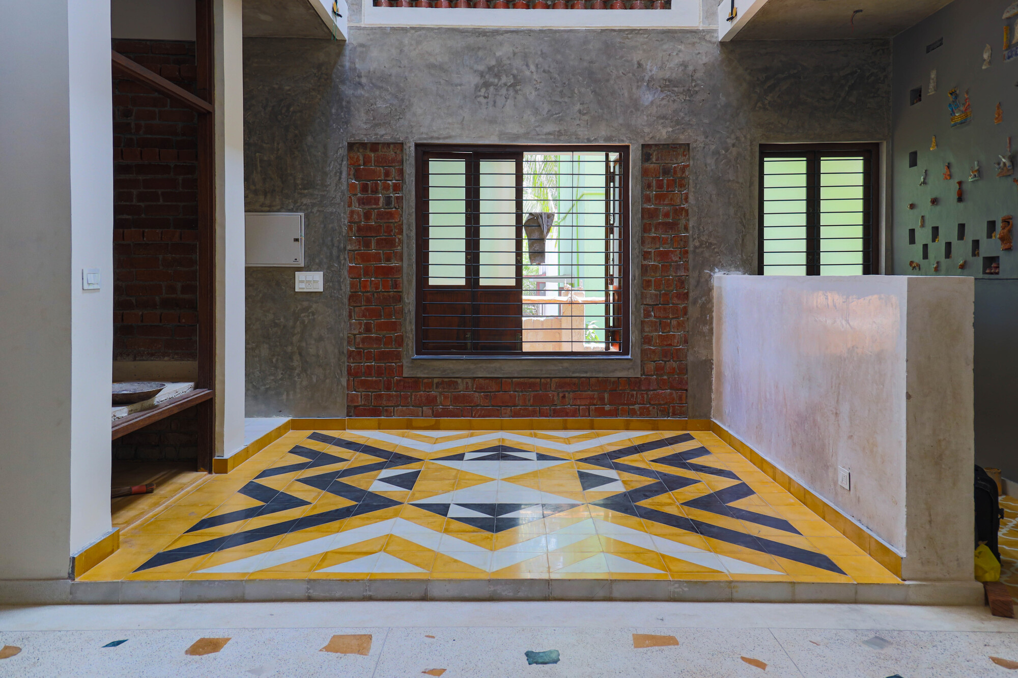 Interior room with geometric yellow and grey floor tiles and exposed brick wall around the window