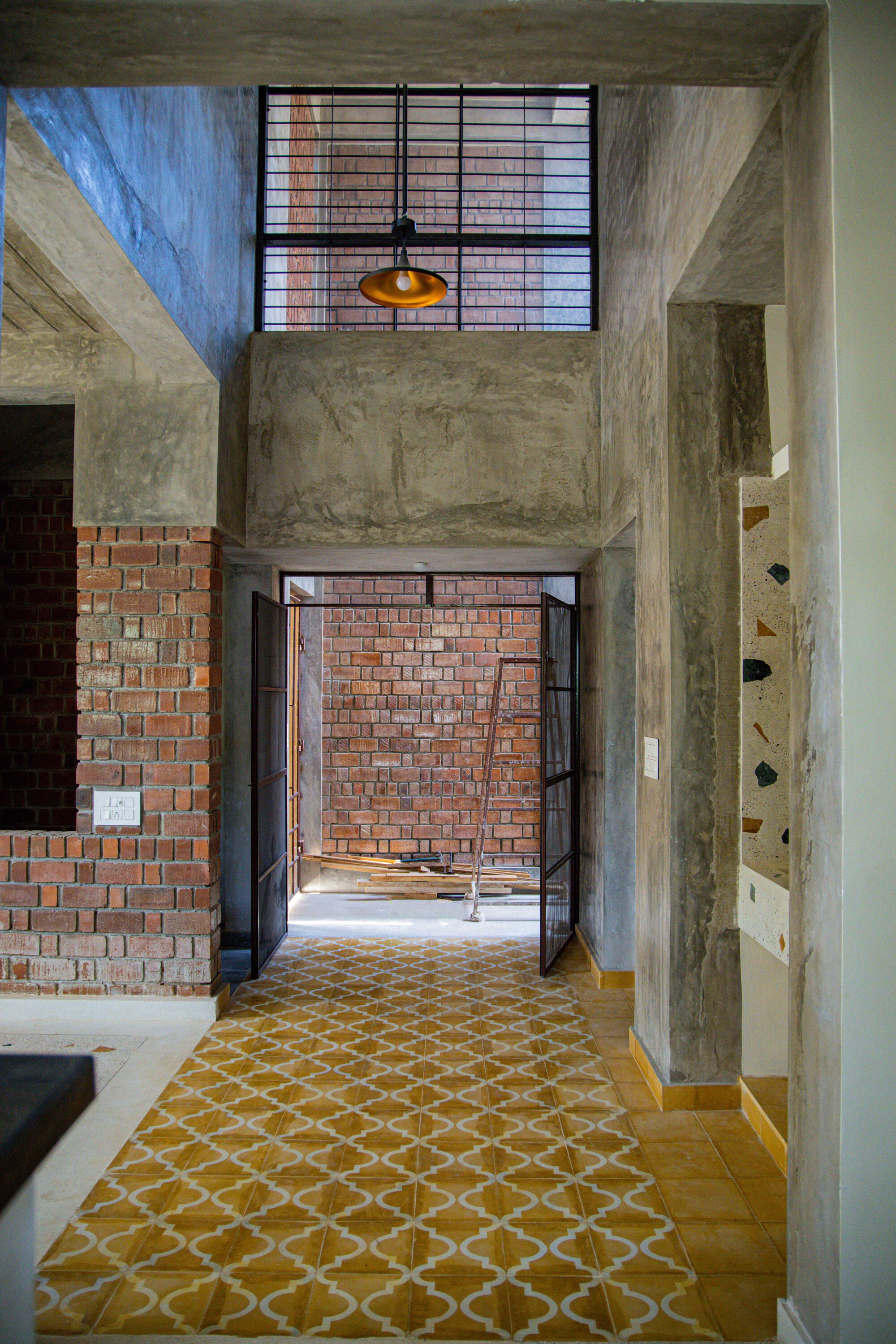 Double-height entryway with yellow patterned floor leading to brick wall and pendant light above