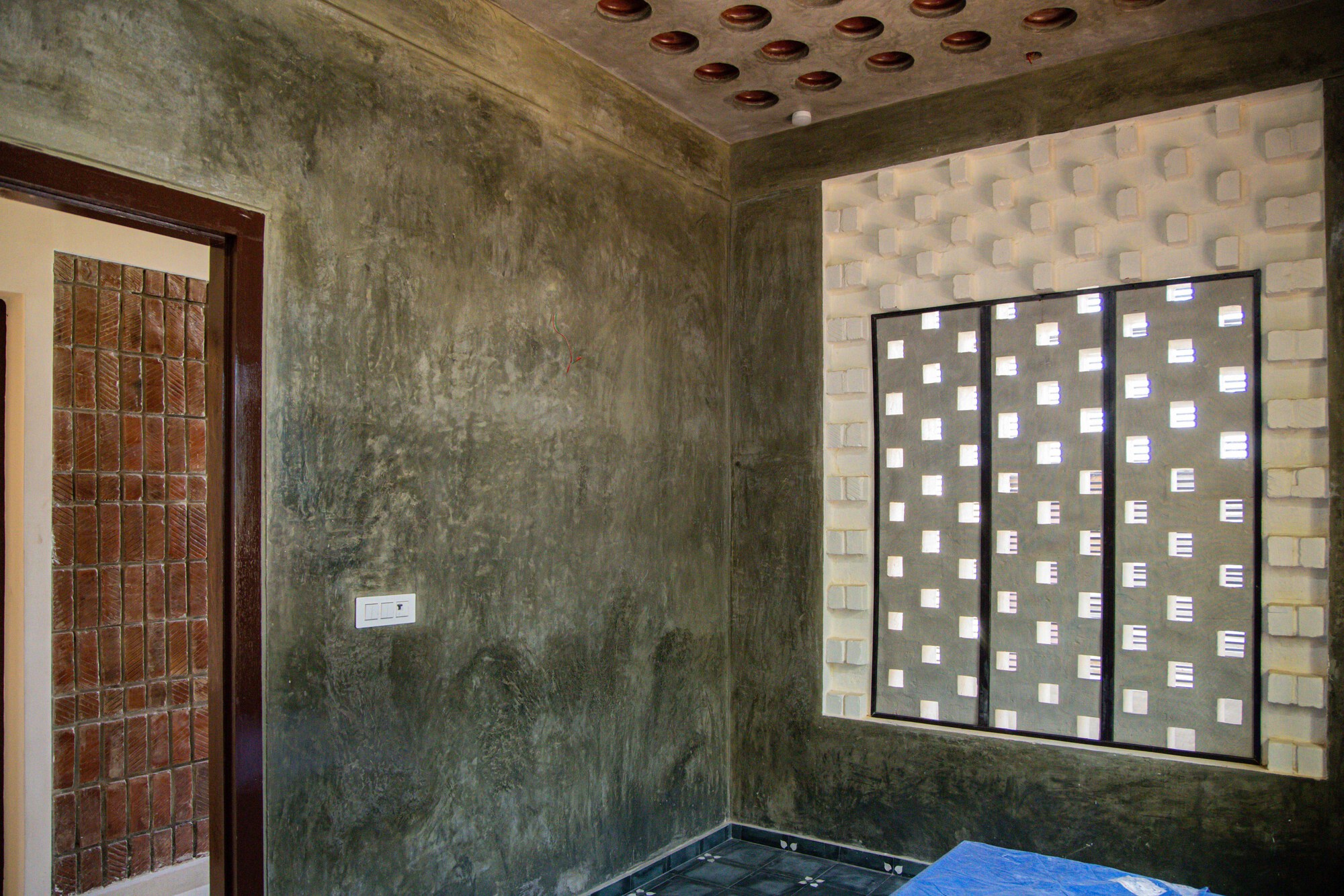 Interior corner showing exposed concrete walls, perforated brick screen door, and patterned ceiling inserts