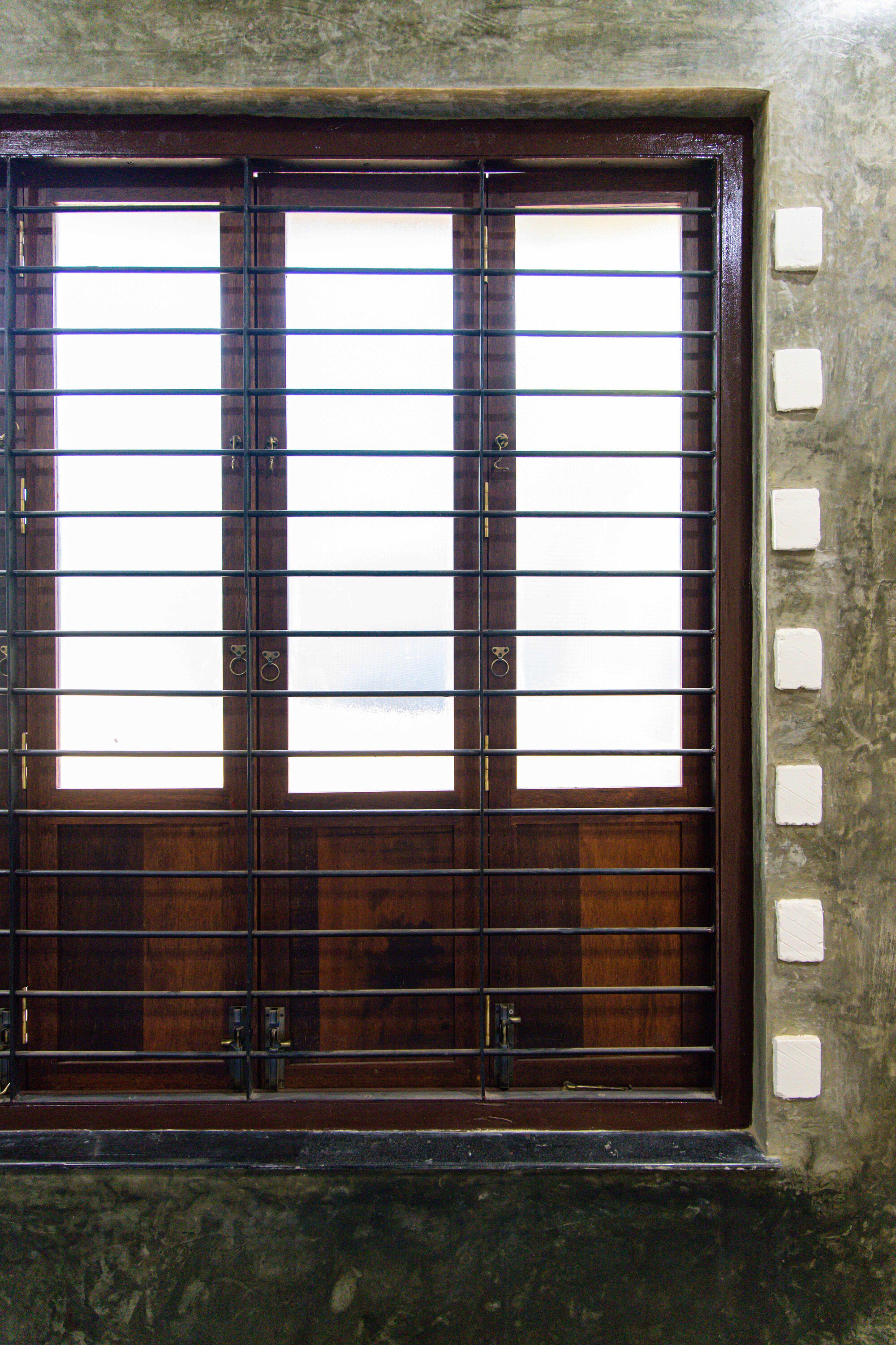 Close-up of dark timber shuttered window with horizontal metal bars against a concrete frame