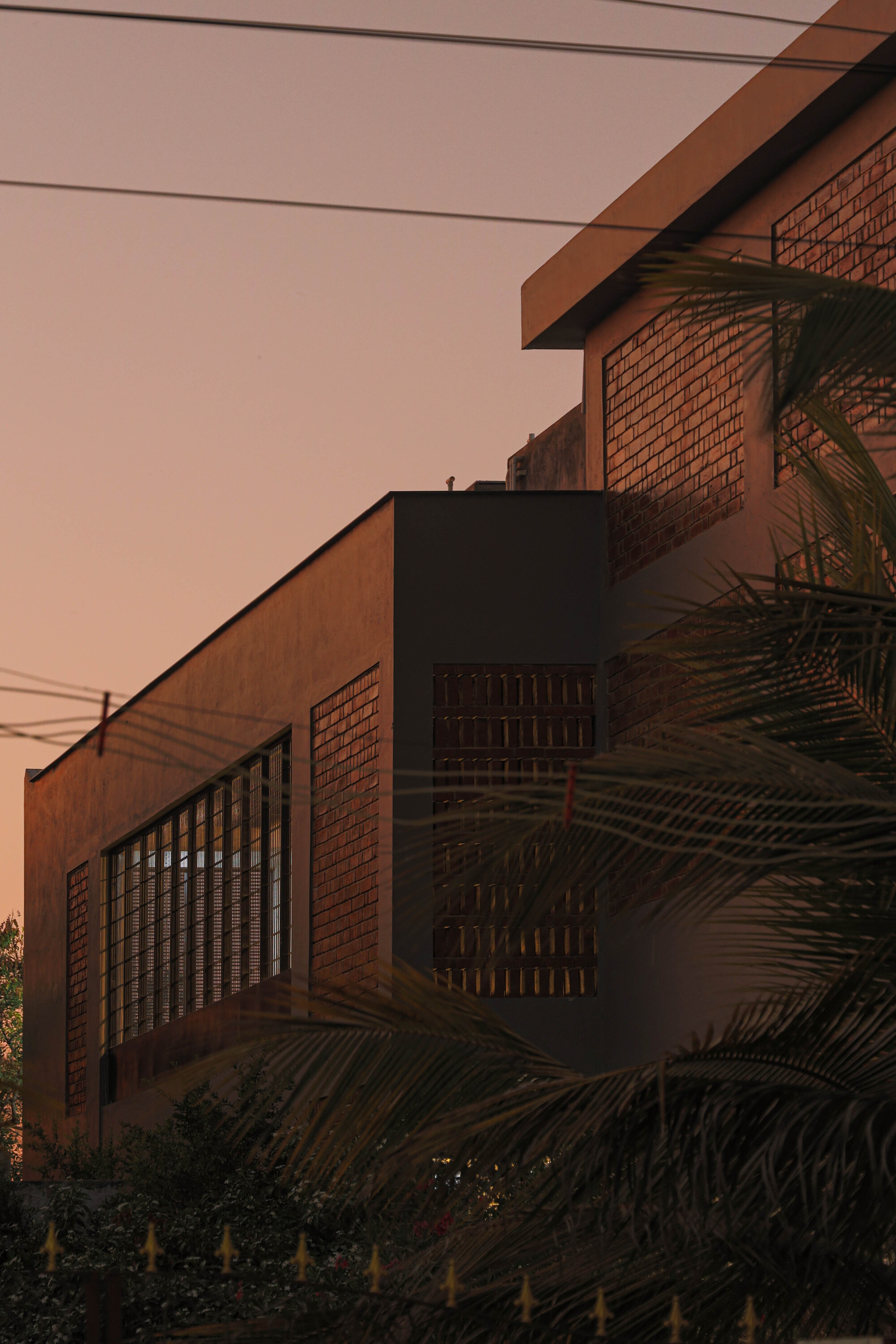 Stacked balconies with brick cladding and lattice screens framed by palm fronds at dusk