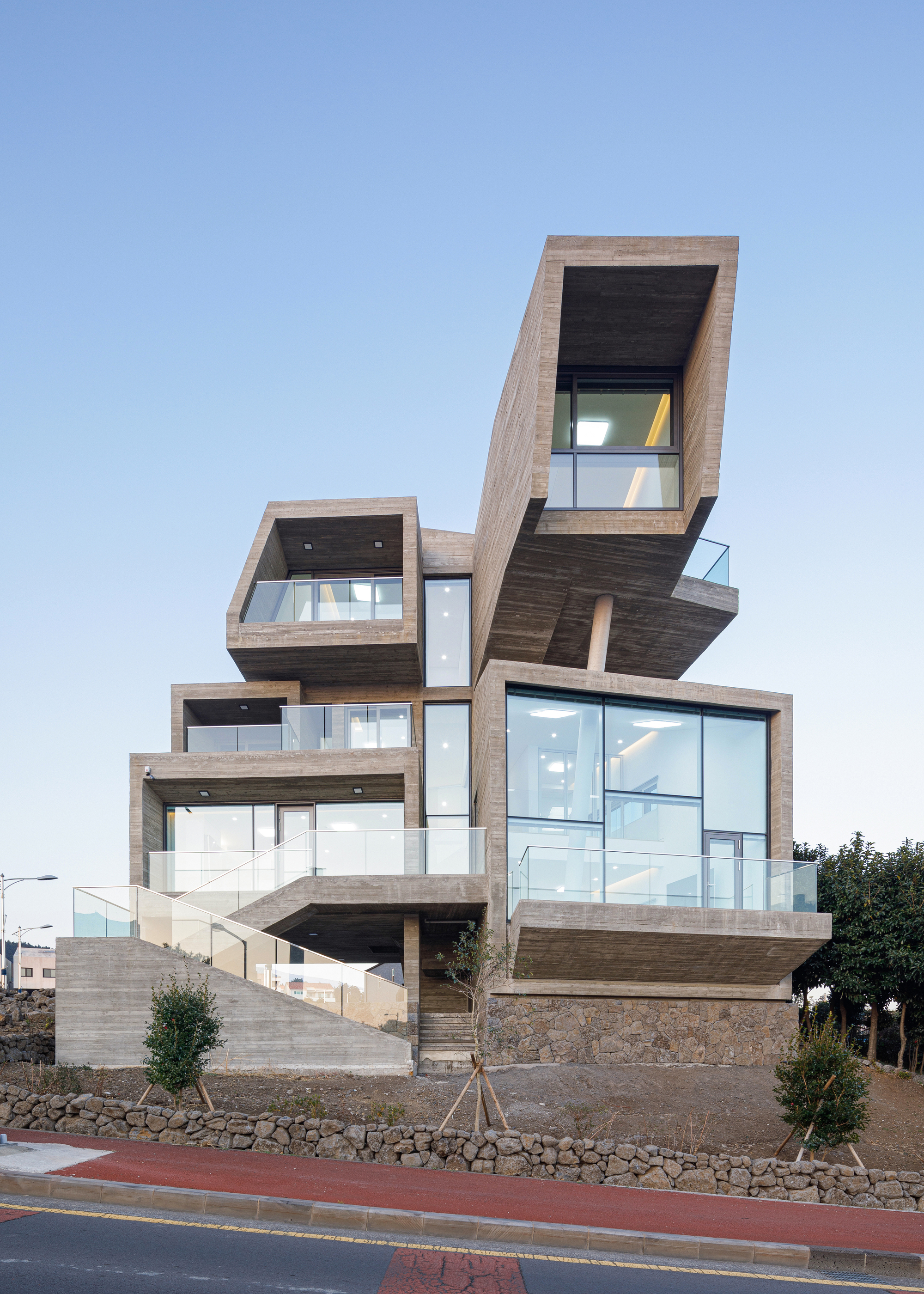 Facade of offset volumes in board-formed concrete with glass balconies and young trees below