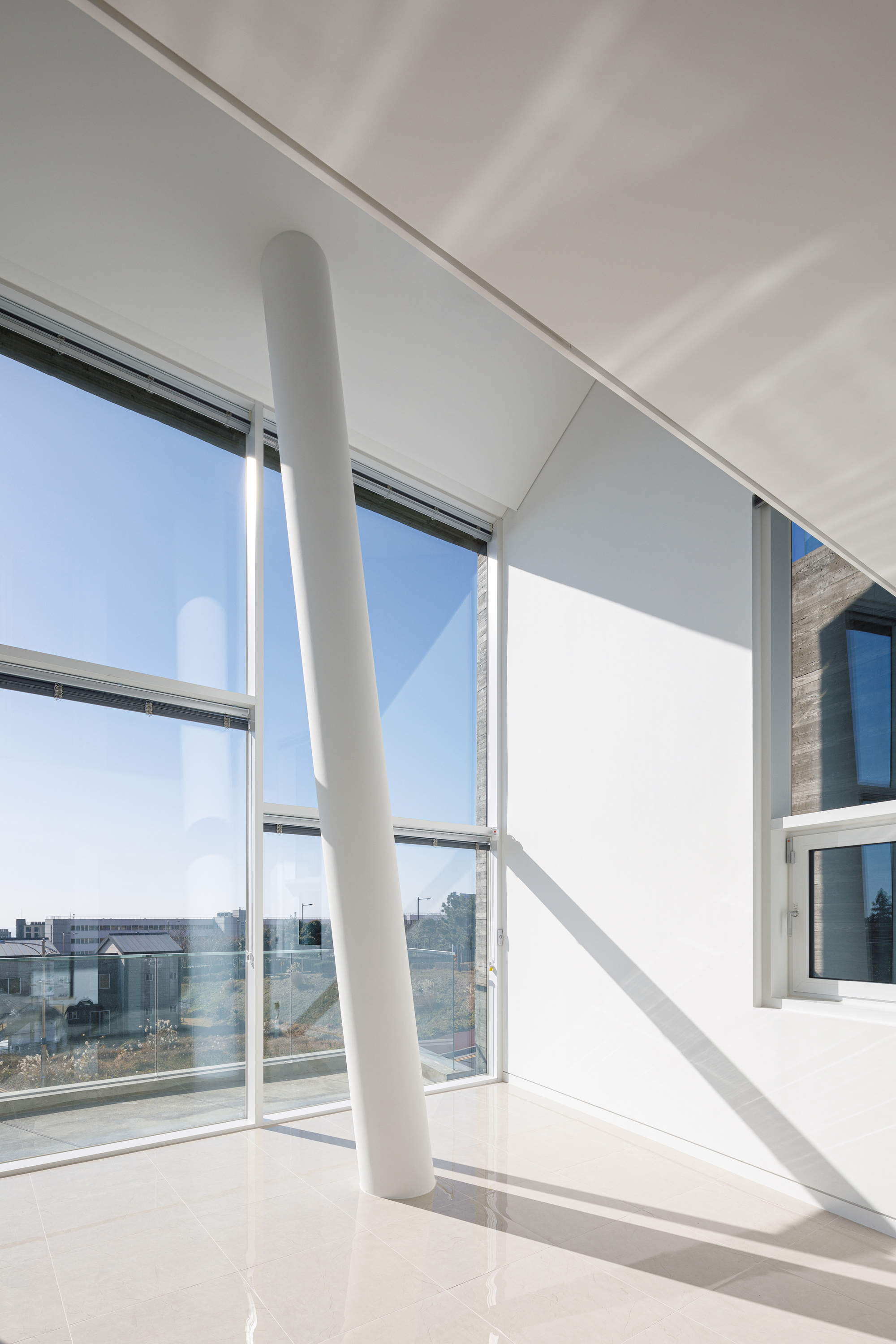 Double-height interior space with a white cylindrical column and full-height glazing casting angular shadows