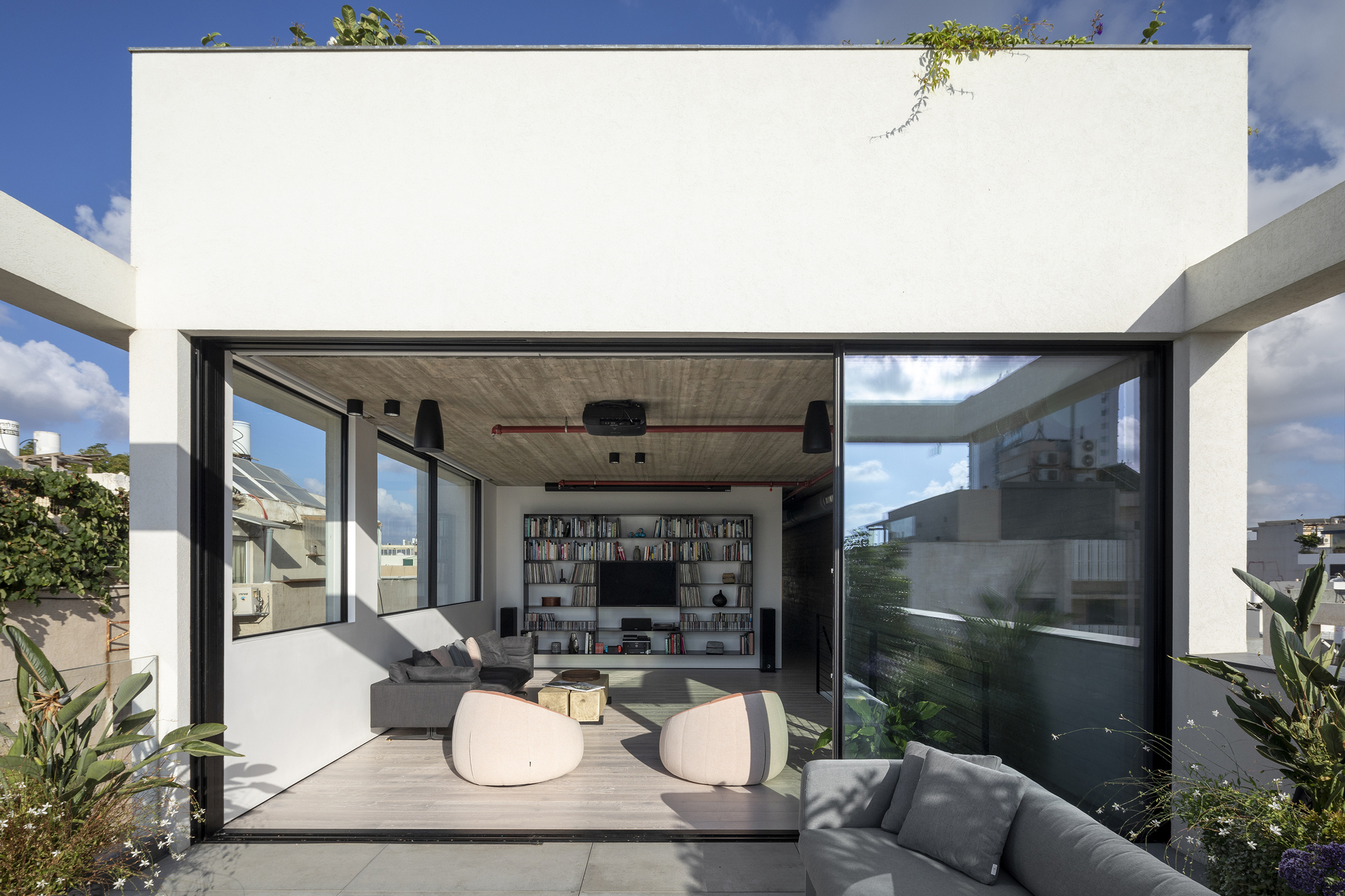 Sliding glass doors opening the living room to a rooftop terrace with plants and blue sky