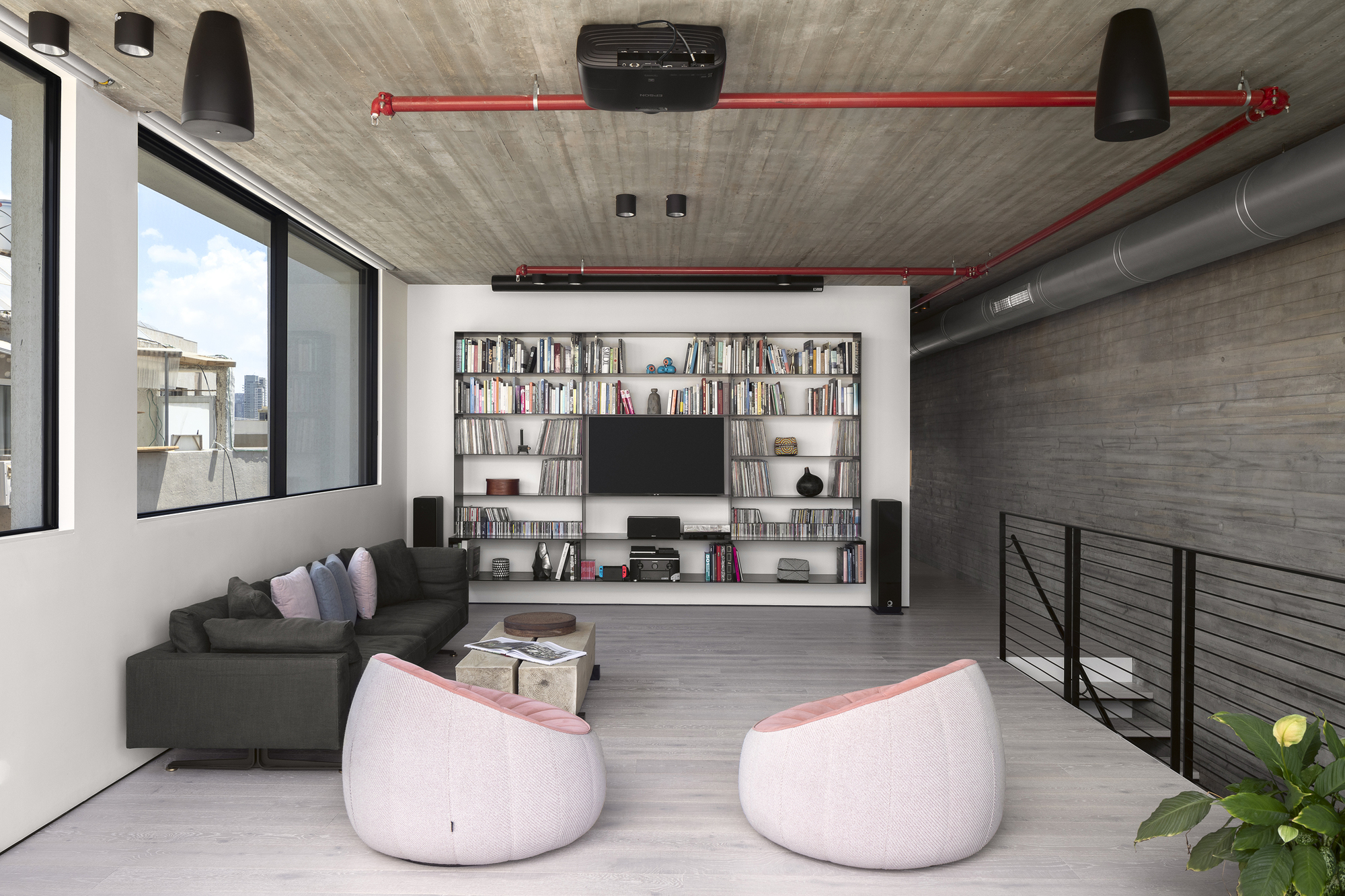 Living room with built-in bookshelf wall, exposed red fire suppression piping, and board-formed concrete ceiling