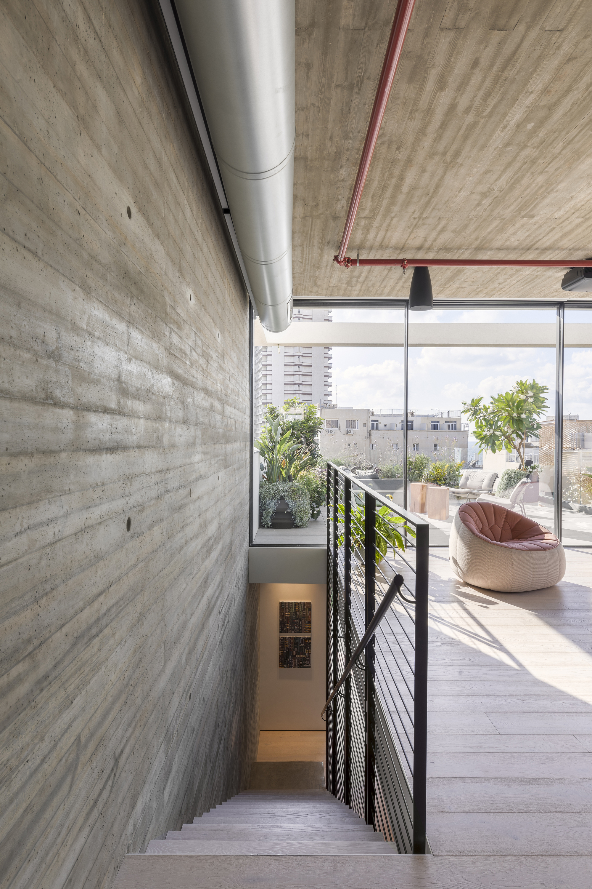 View down the steel staircase with wire railing toward the terrace and potted citrus trees