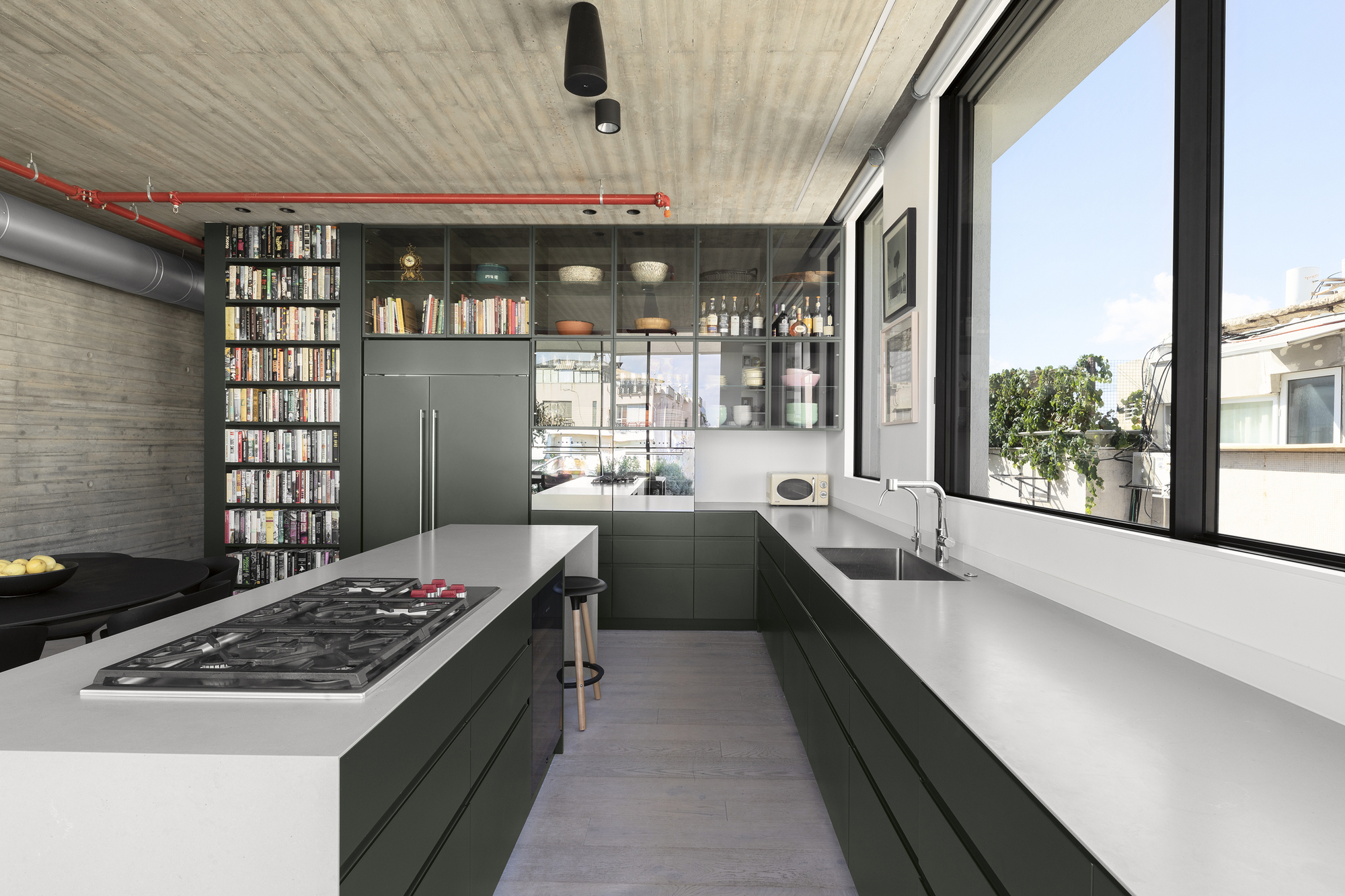 Galley kitchen with dark green cabinetry and white countertops beneath board-formed concrete ceiling and exposed ductwork