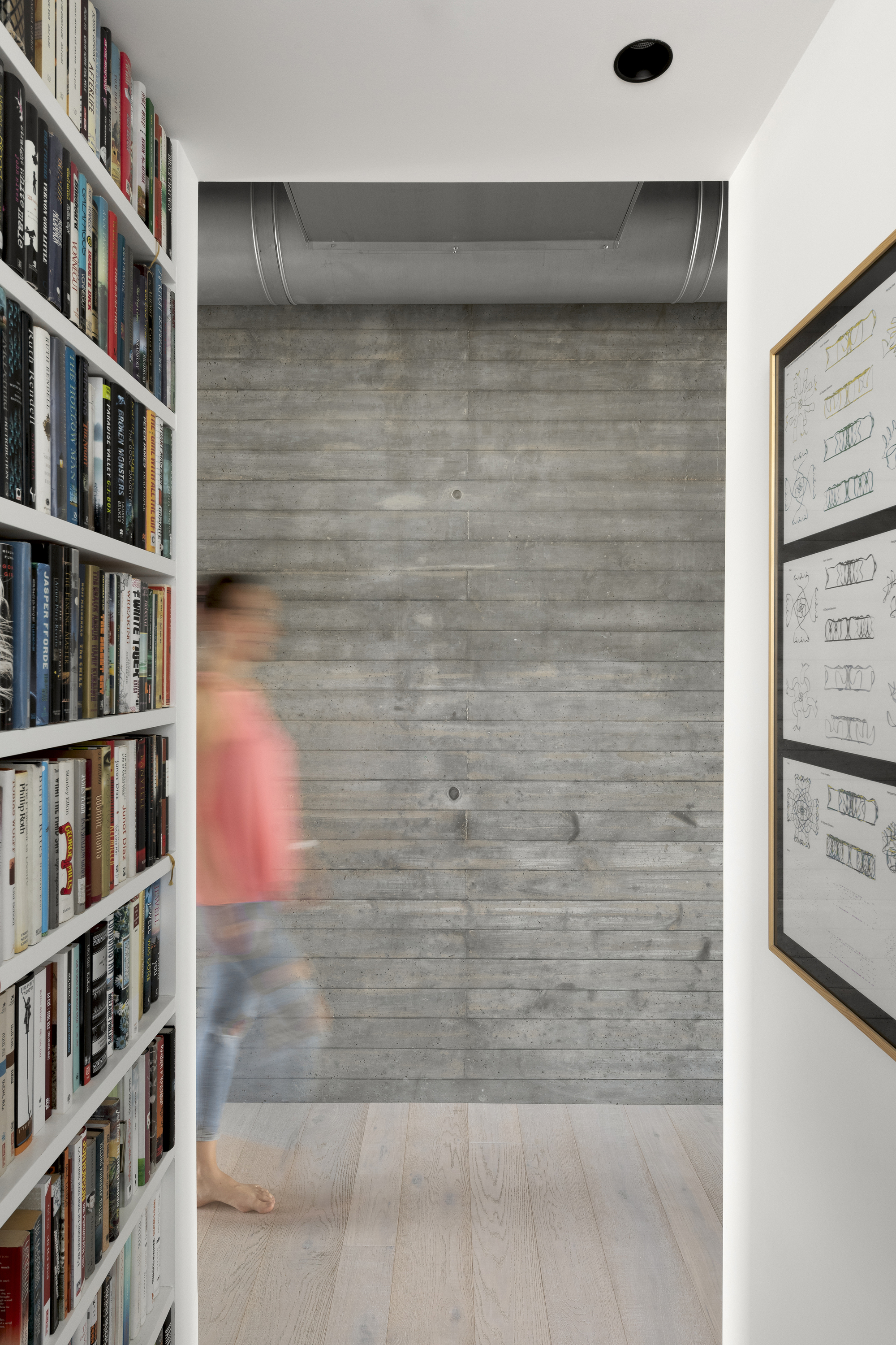 Hallway with board-formed concrete end wall and white bookshelves flanking a figure in motion blur