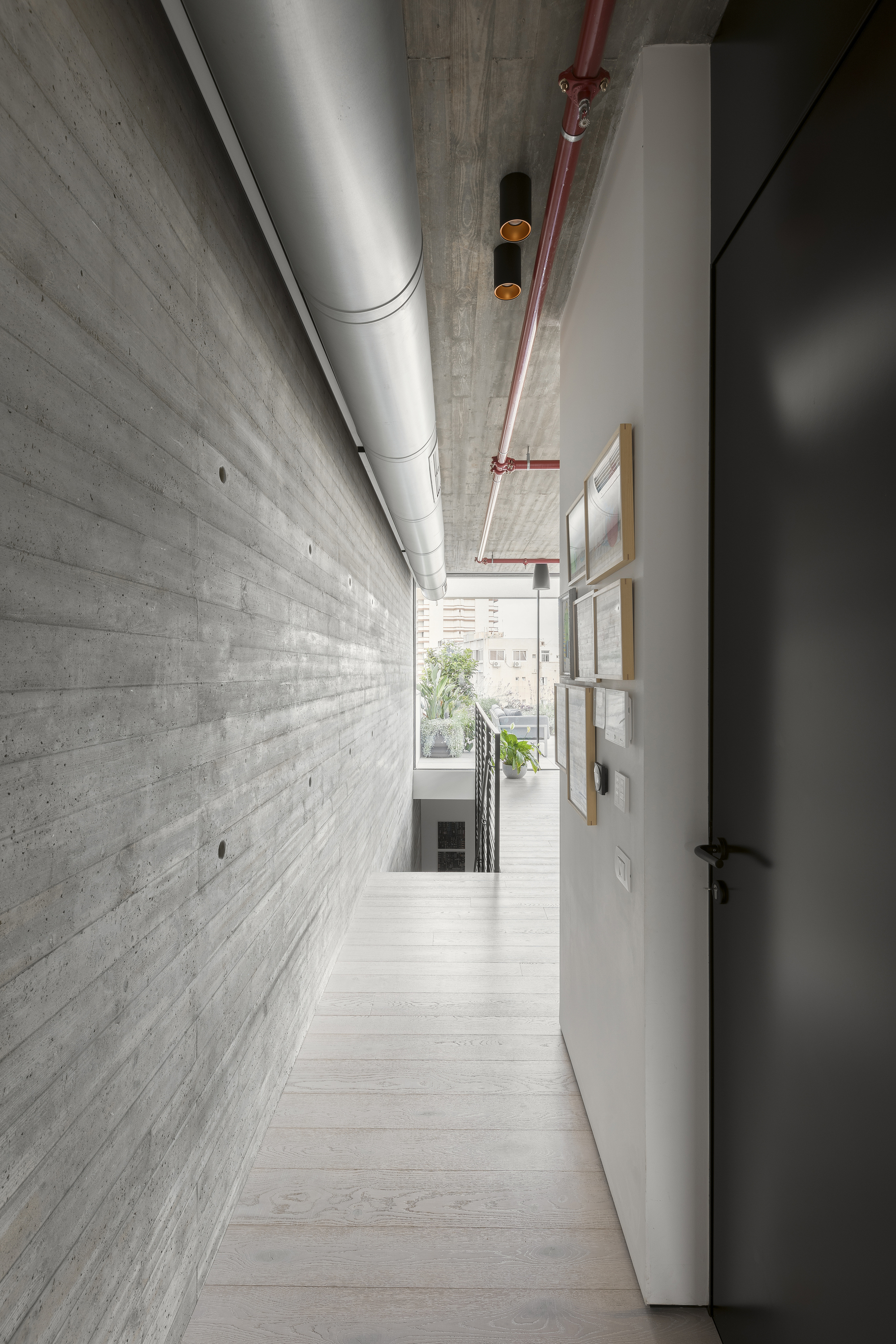 Narrow corridor with board-formed concrete wall alongside exposed HVAC ductwork and red fire suppression piping