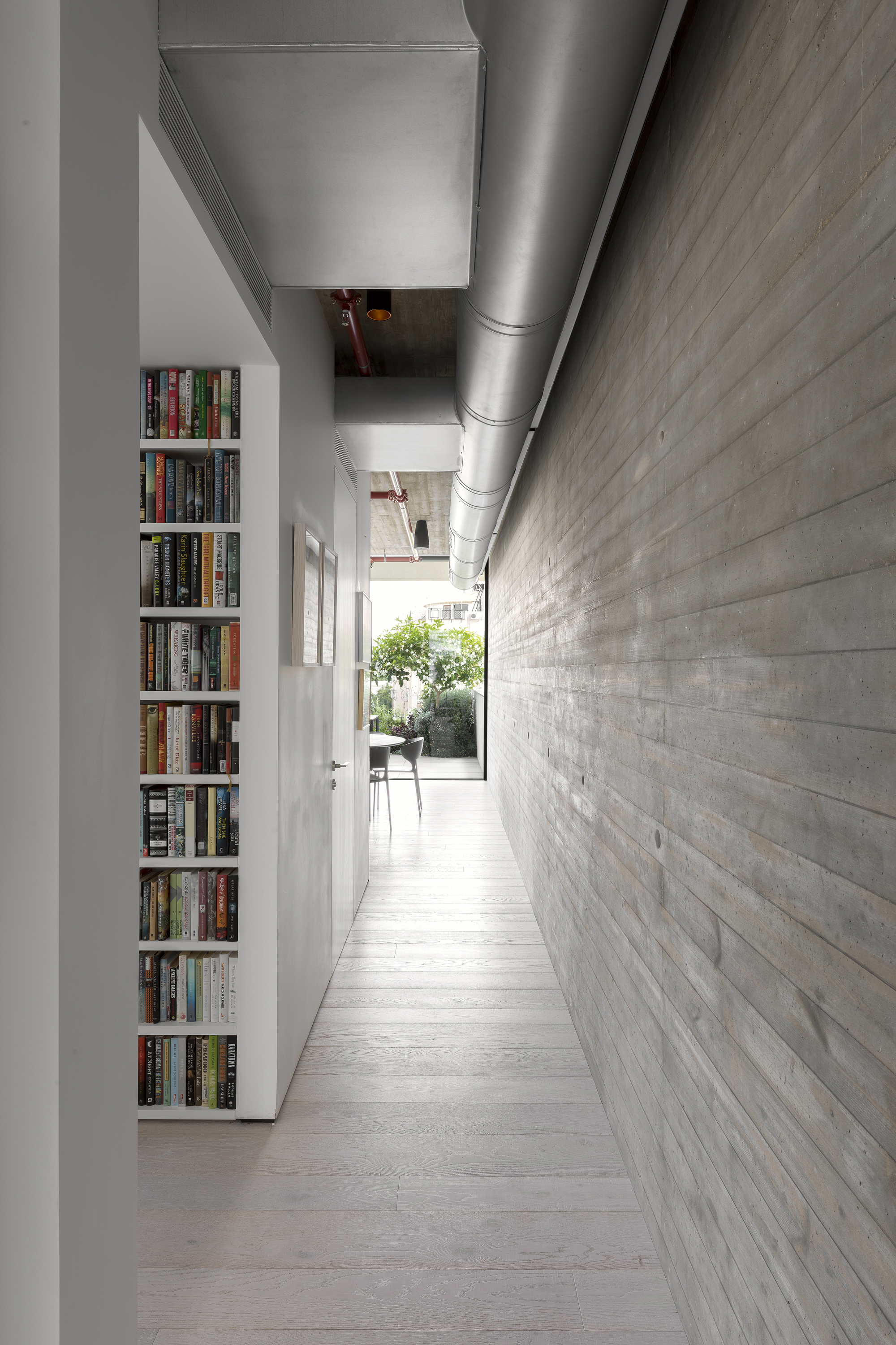 Narrow corridor with exposed ductwork above and horizontal board-formed concrete wall with built-in bookshelves